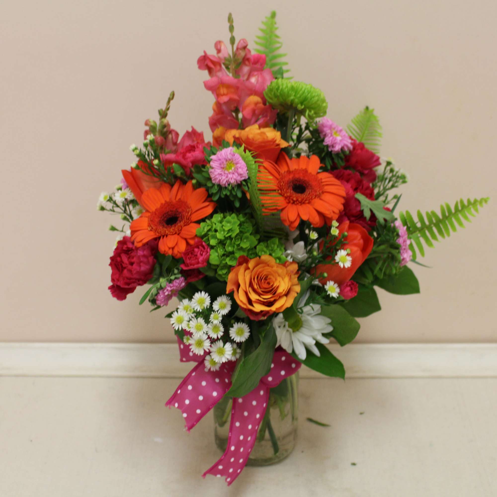 Mixed bouquet of orange and pink flowers in a glass vase with a polka-dot ribbon