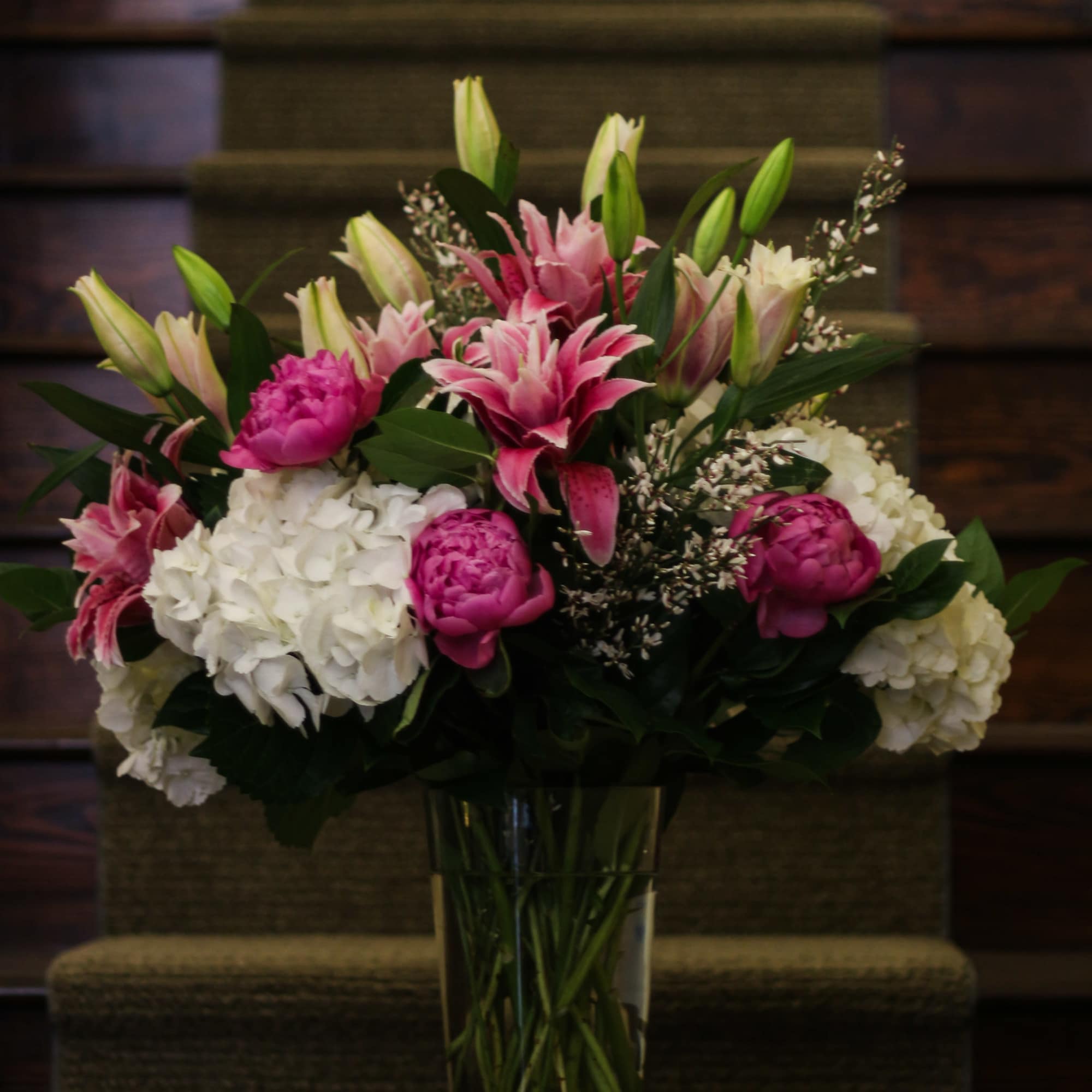 Pink lilies and white hydrangeas arranged in a tall glass vase