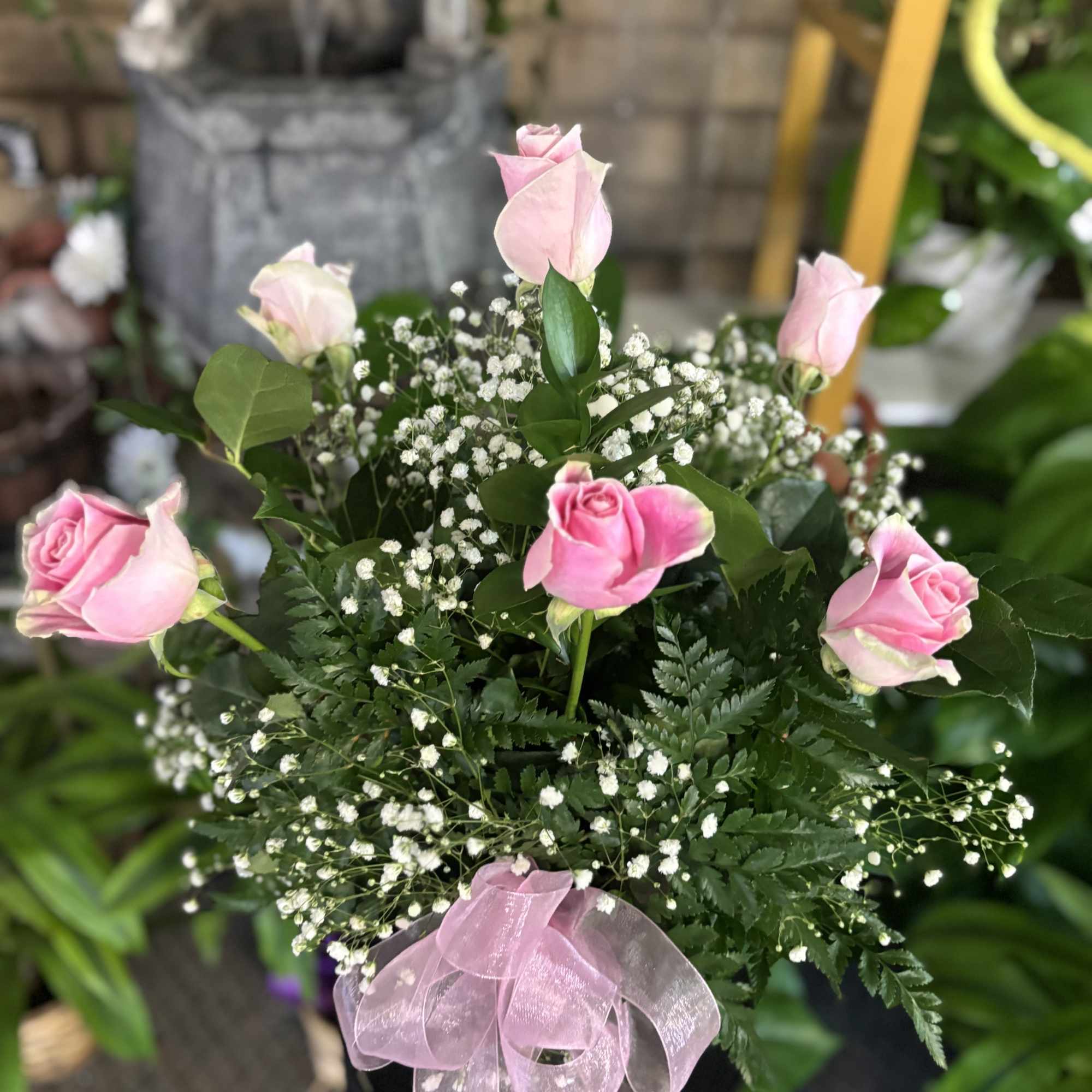 Pink roses arranged with baby's breath in a black container and pink ribbon