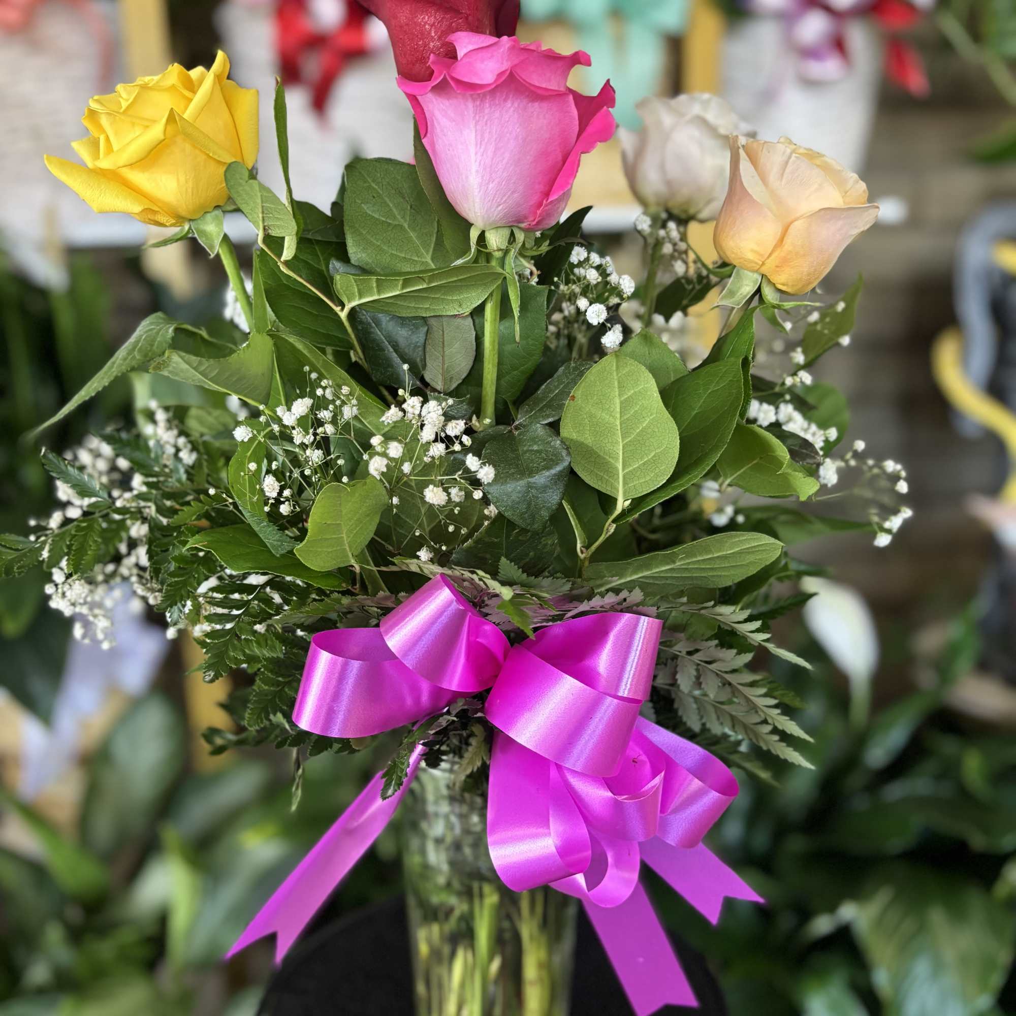 Bouquet of multicolored roses in a glass vase with a pink ribbon