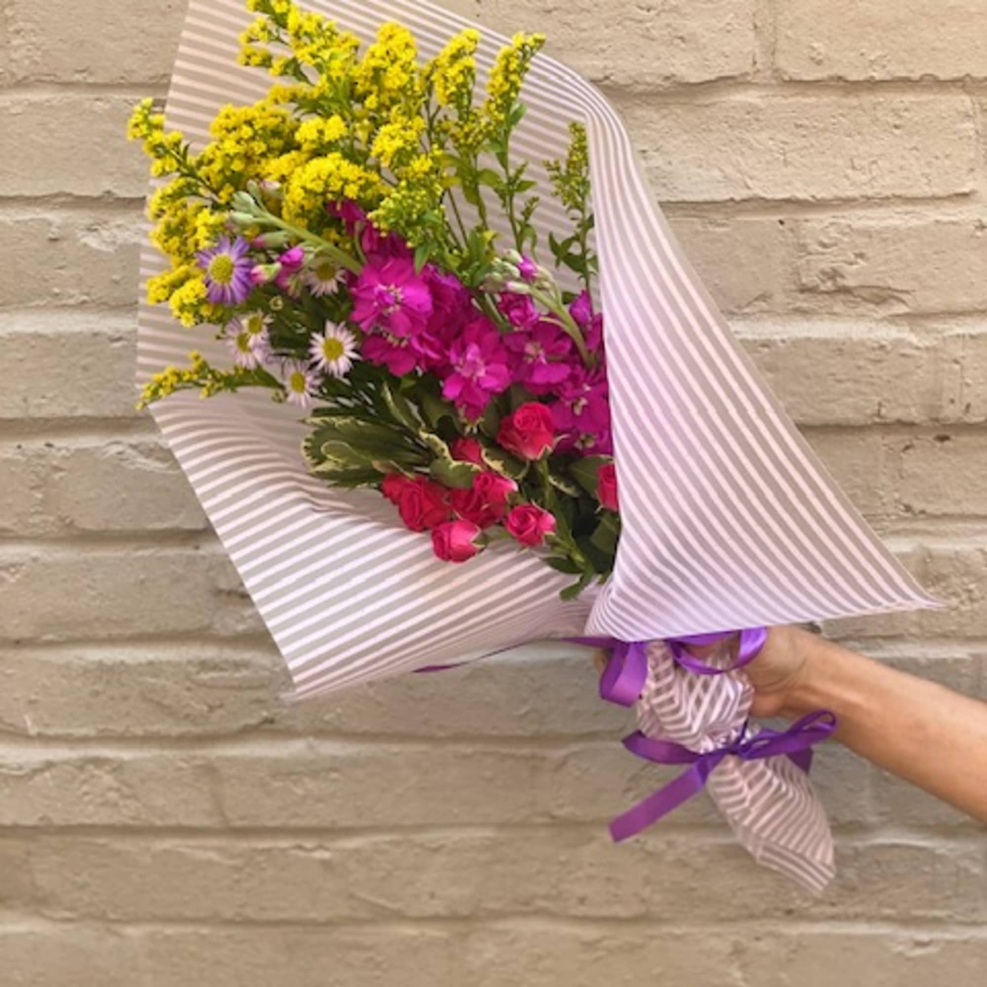 Hand-tied bouquet of yellow, pink, and purple flowers in striped wrap