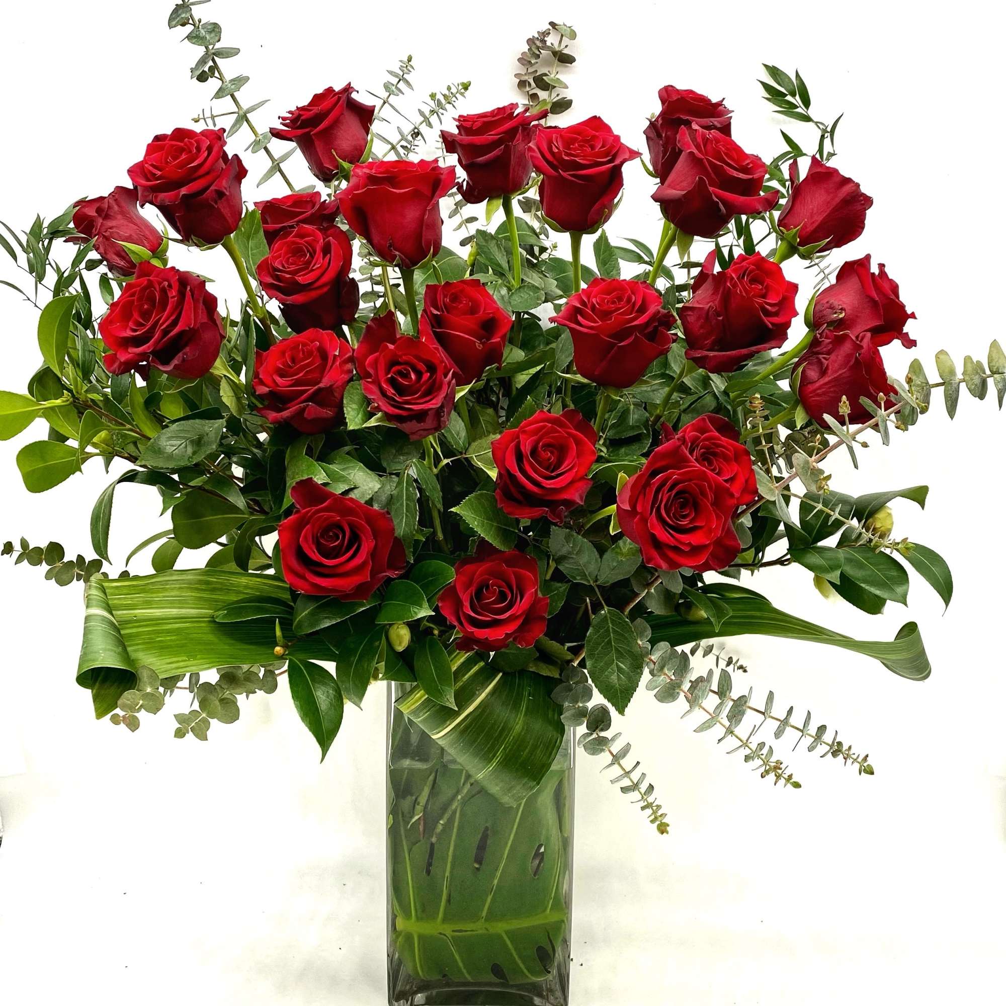 Red roses arranged in a clear glass vase with eucalyptus and broad leaves