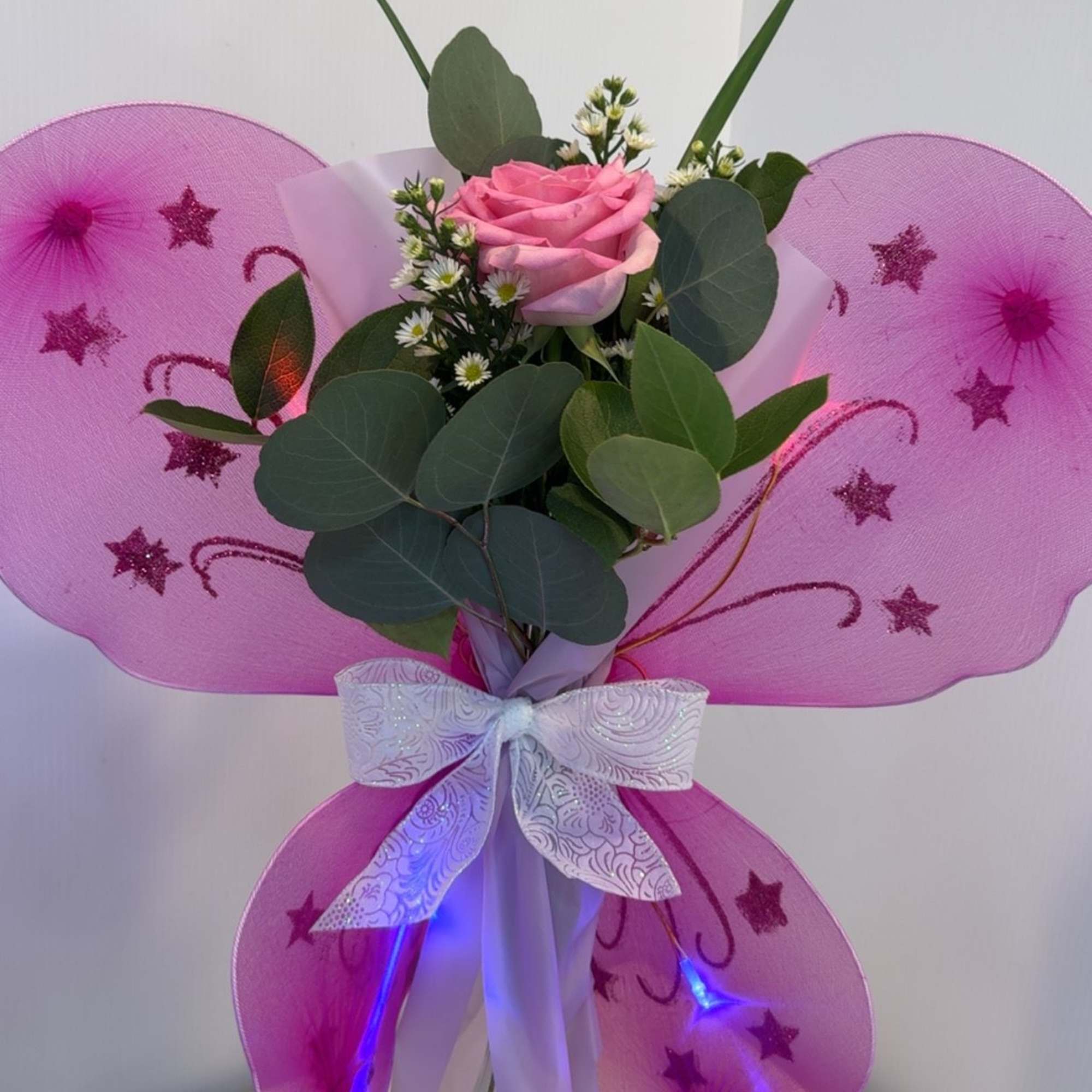 A rose or Gerber accented with fresh greenery, filler, and sparkling butterfly