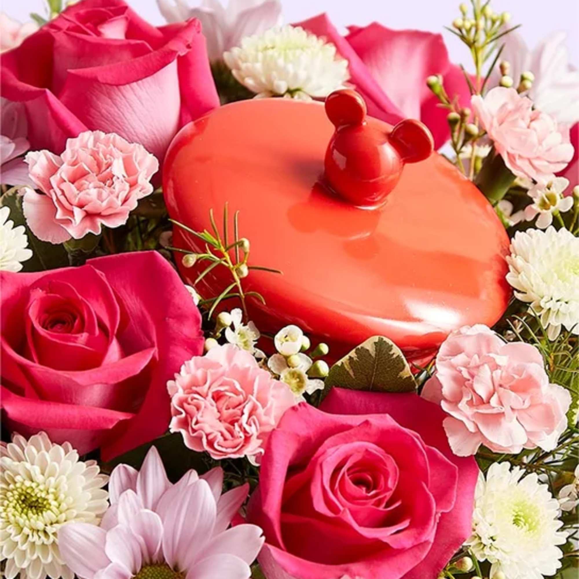 Pink roses and carnations surrounding a red lidded container