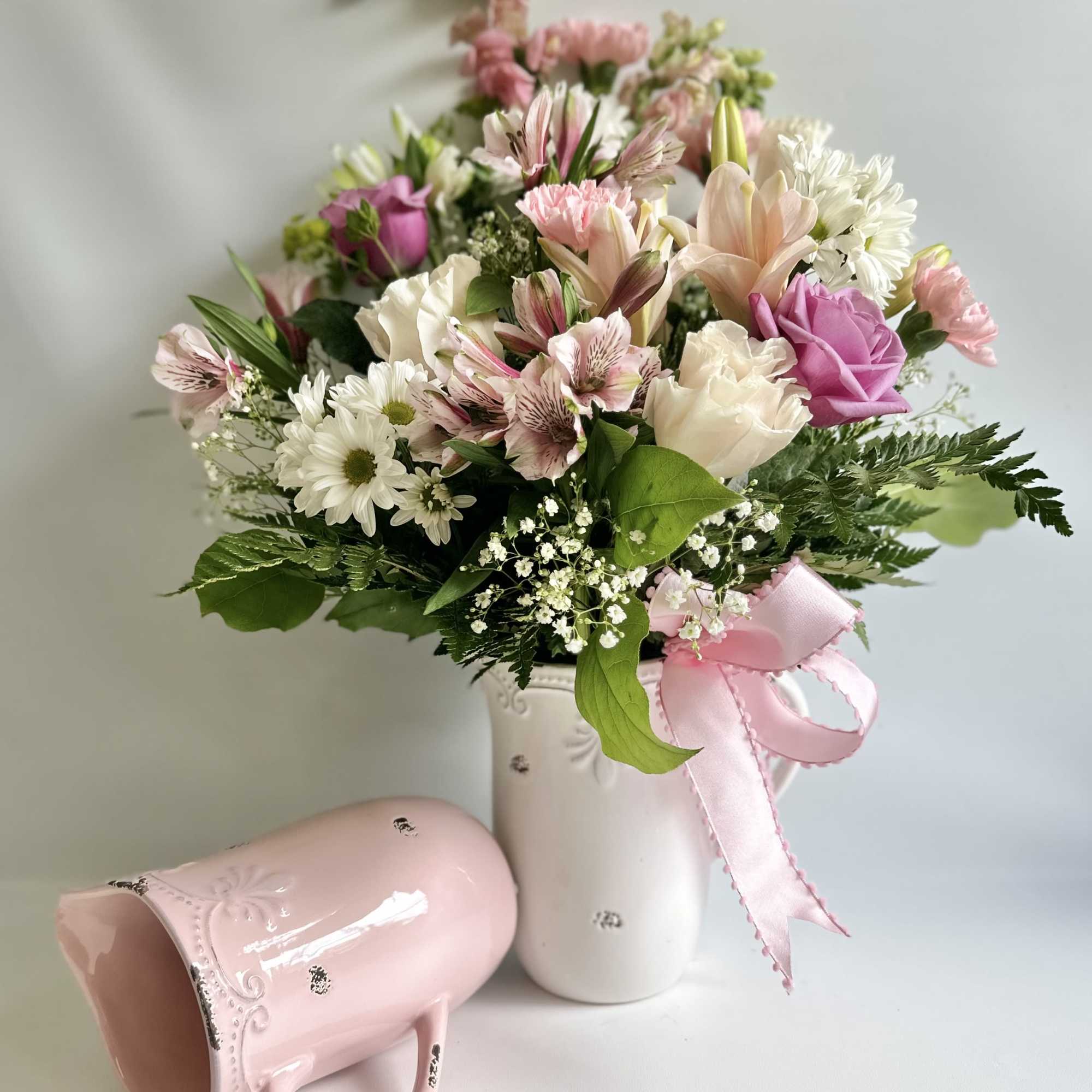 Pink and white mixed bouquet in a white vase with a pink ribbon