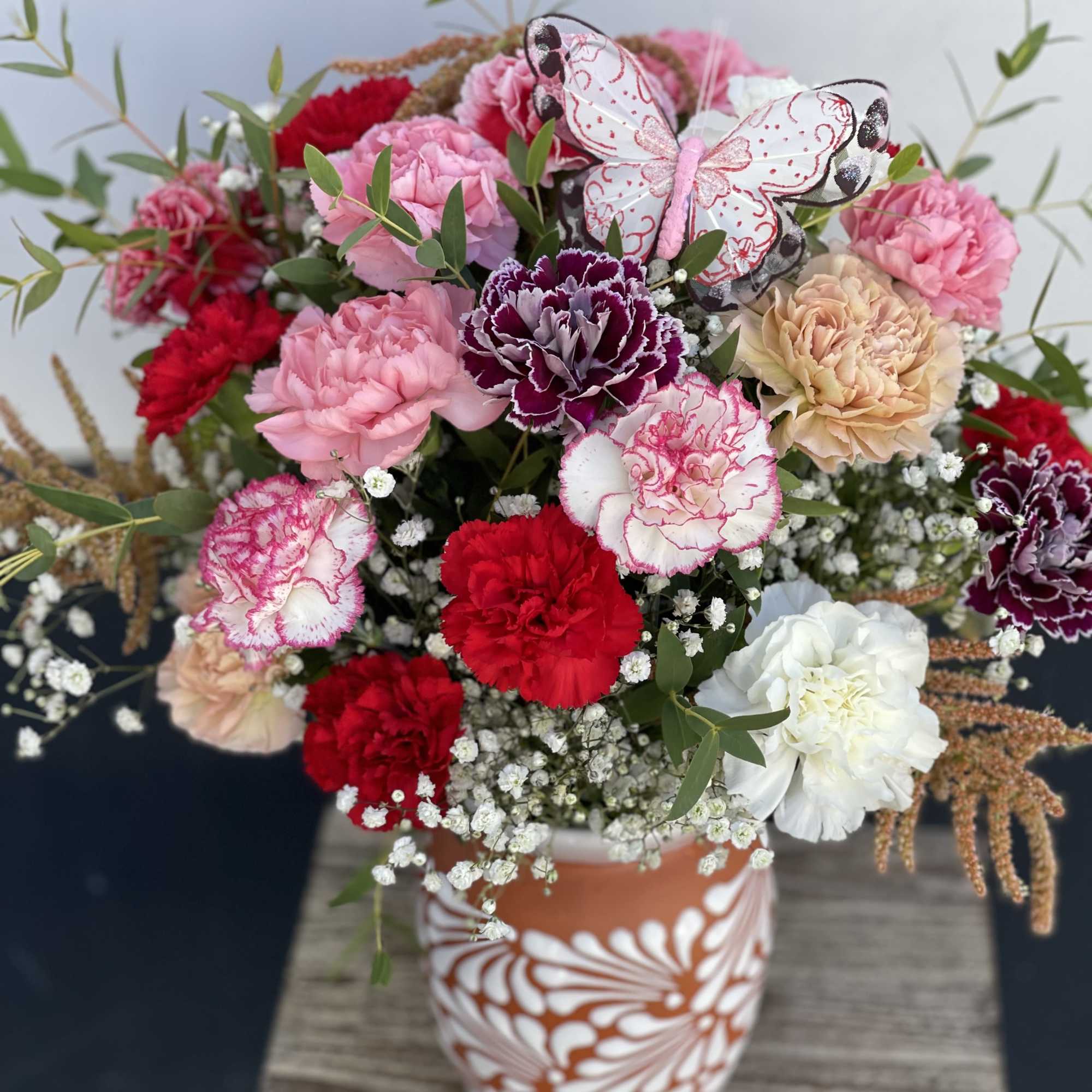 Mixed bouquet of pink, red, and white carnations in a patterned vase