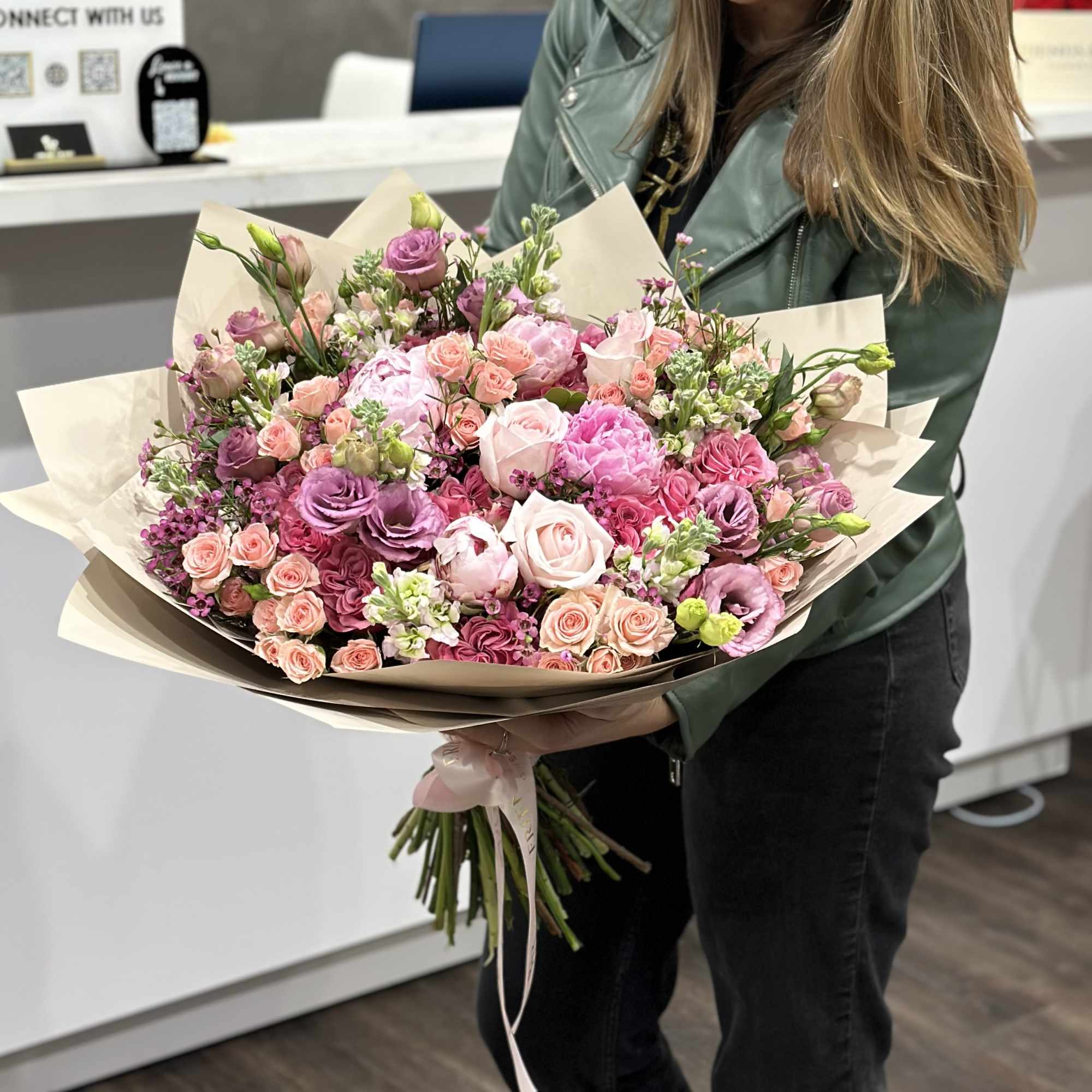Large bouquet of pink and lavender roses with mixed blooms wrapped in paper