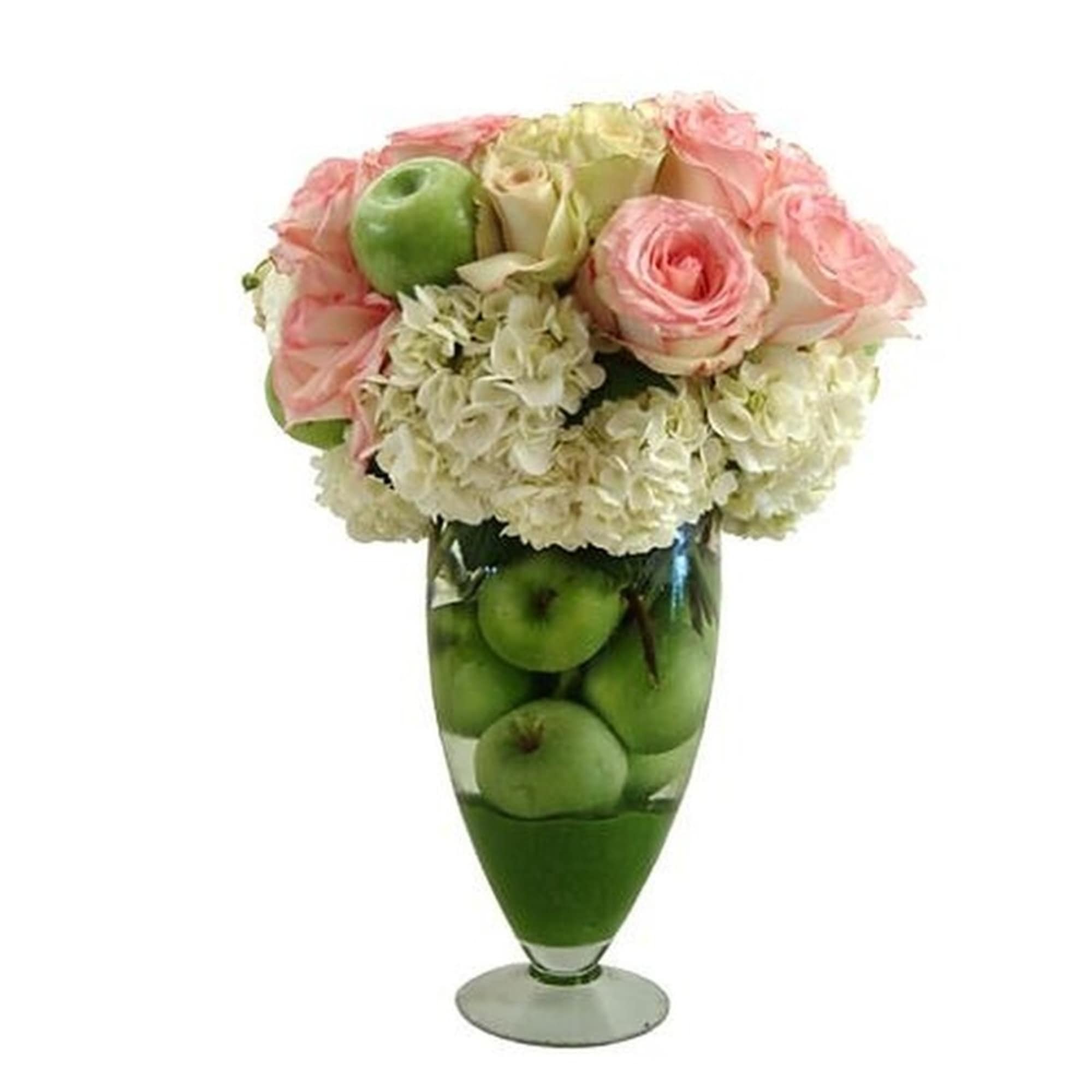 Tall glass vase filled with green apples topped with white hydrangeas and pink roses