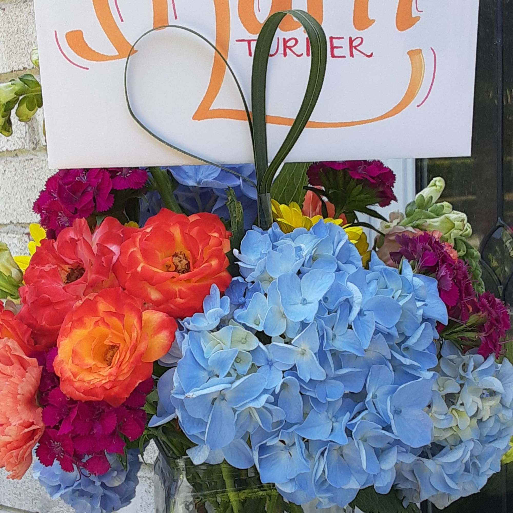 Colorful mixed bouquet in a clear glass vase with a sign behind it