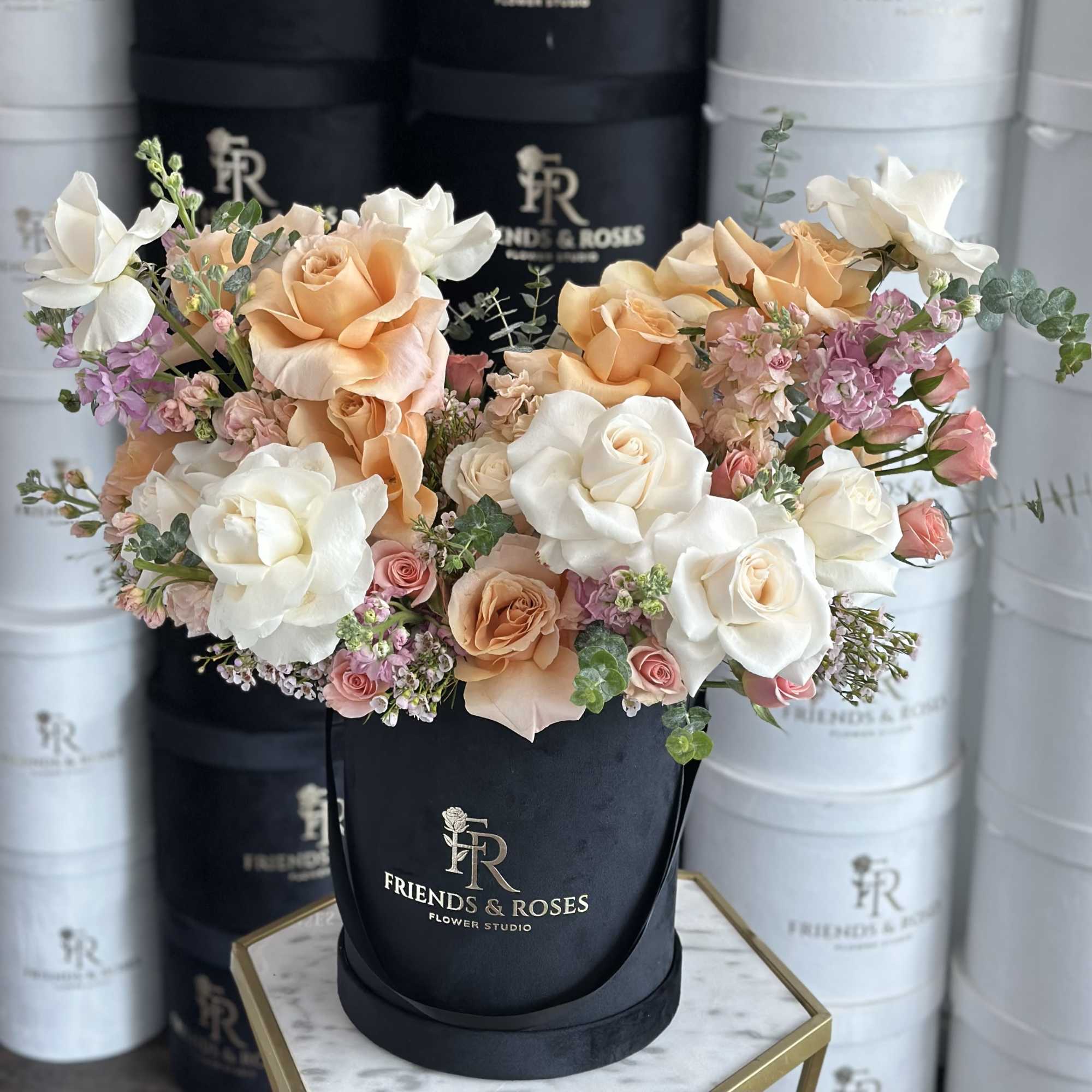 Peach and white roses arranged in a black hatbox