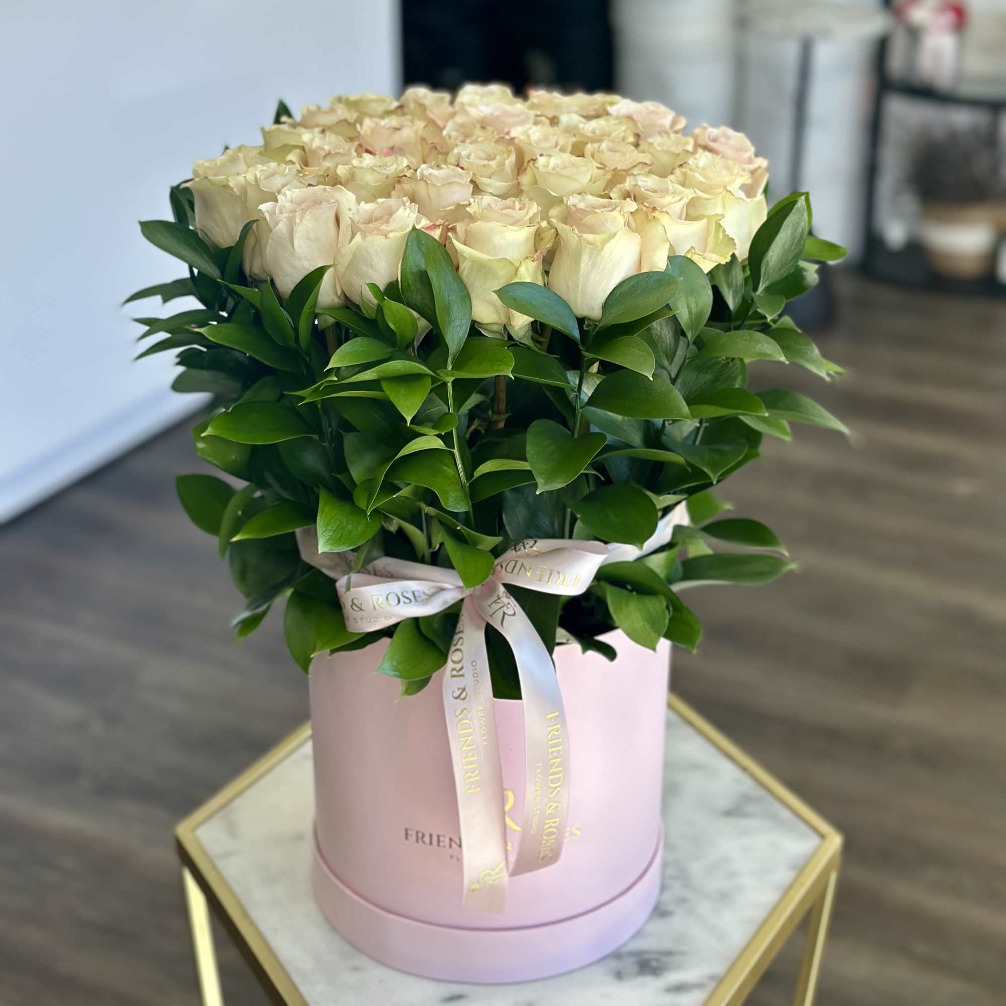 Cream roses arranged in a pink hat box with a ribbon