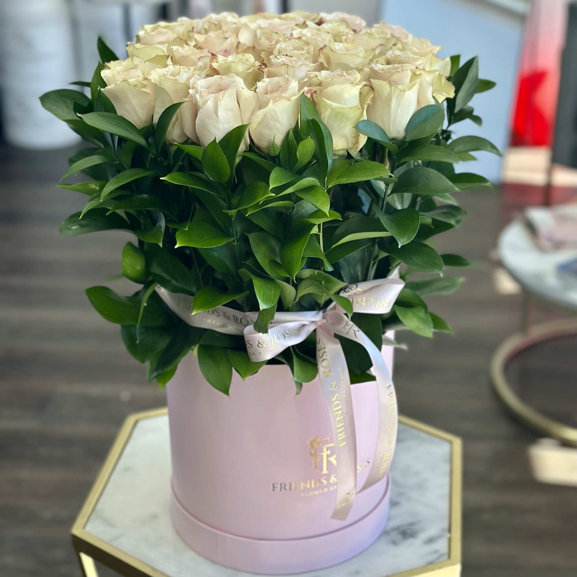 Cream roses arranged in a pink hat box with a ribbon.