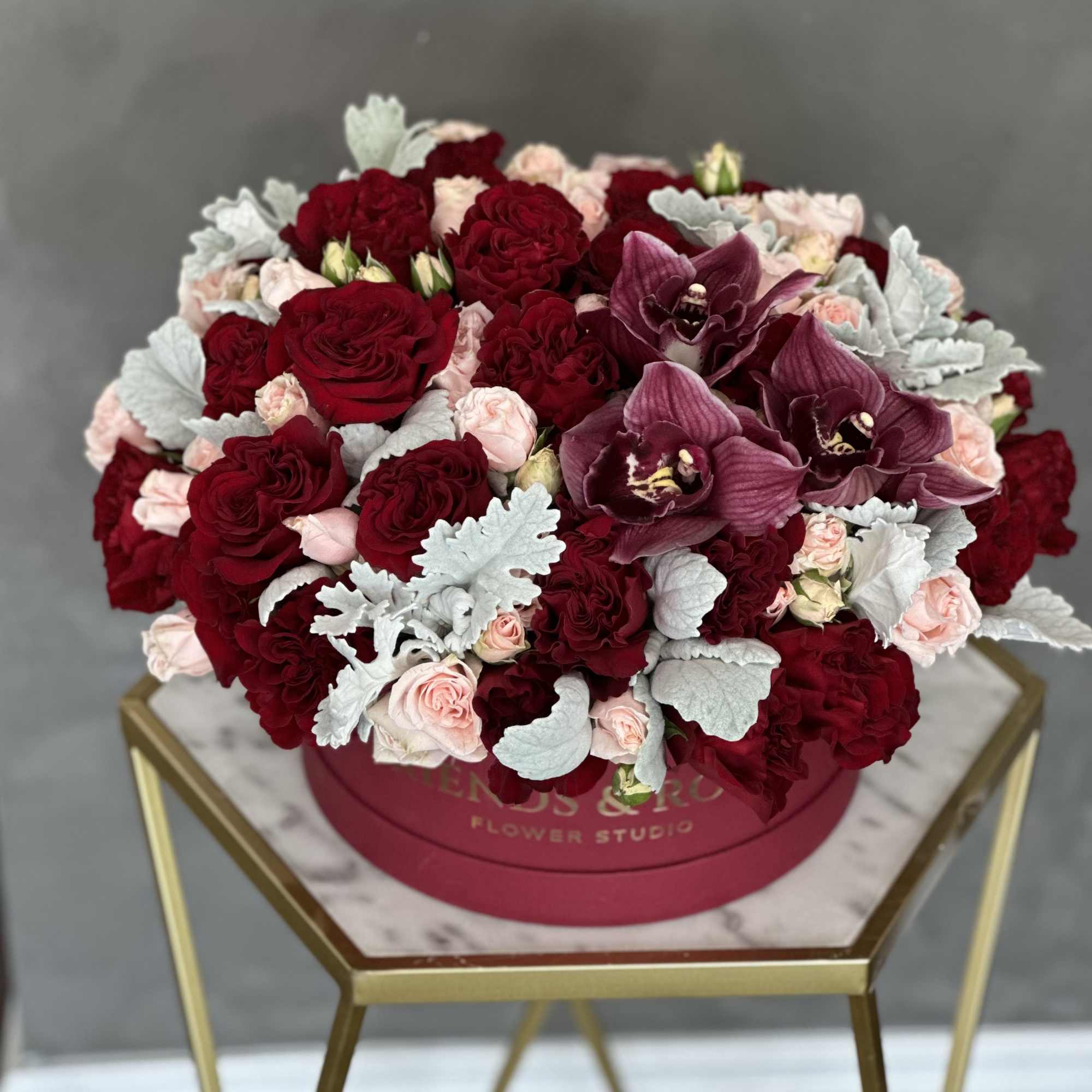 Round bouquet of red and blush roses with purple orchids in a pink box