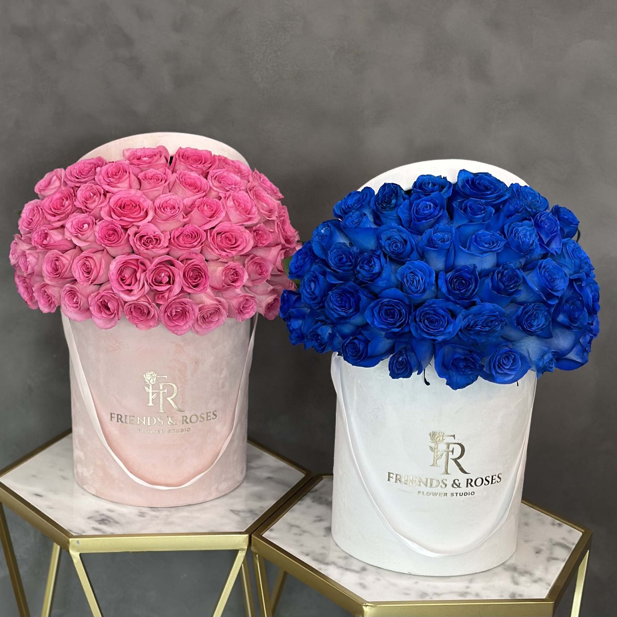 Two hatbox arrangements of roses, one pink and one blue.