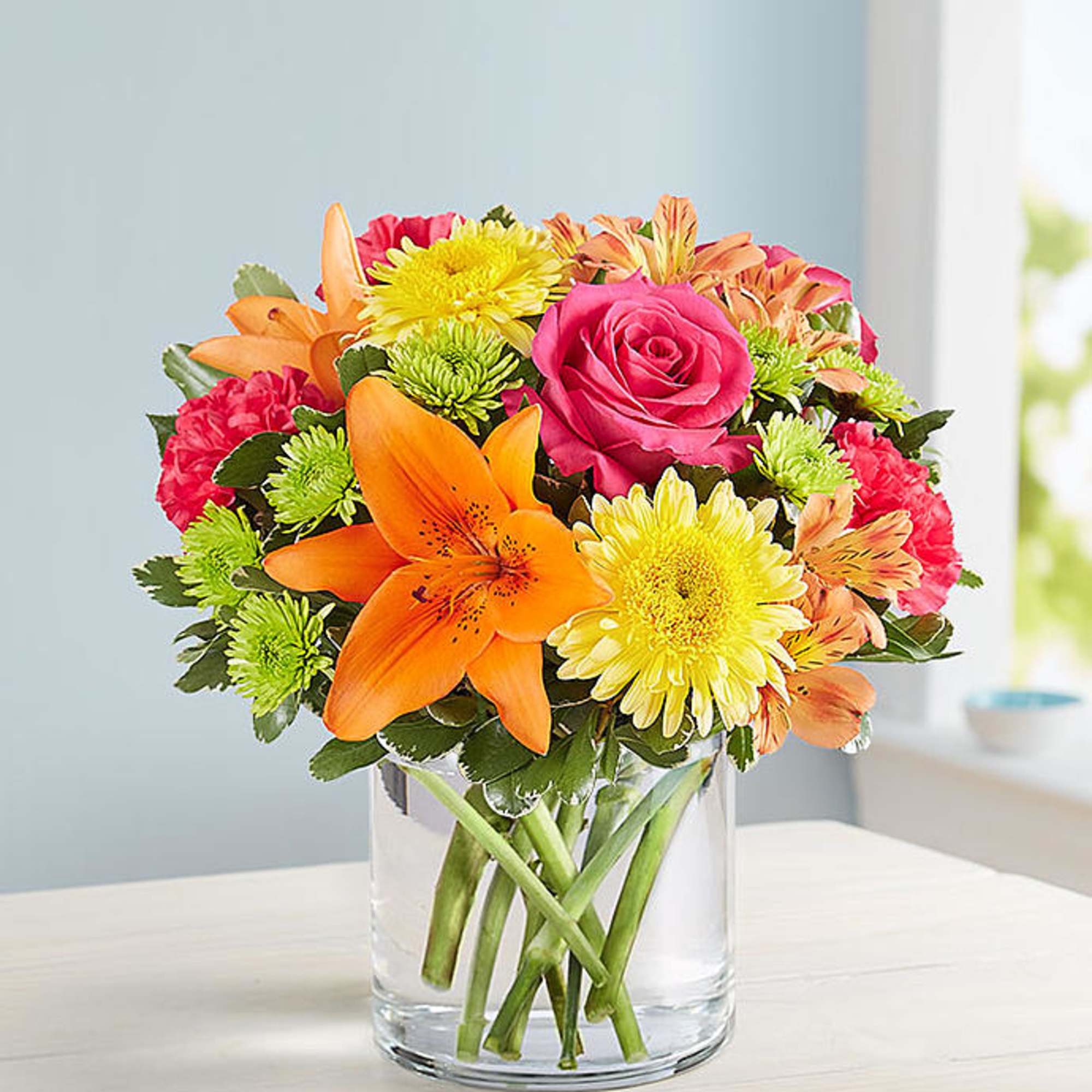 Bouquet of orange lilies, pink roses, and yellow daisies in a clear glass vase