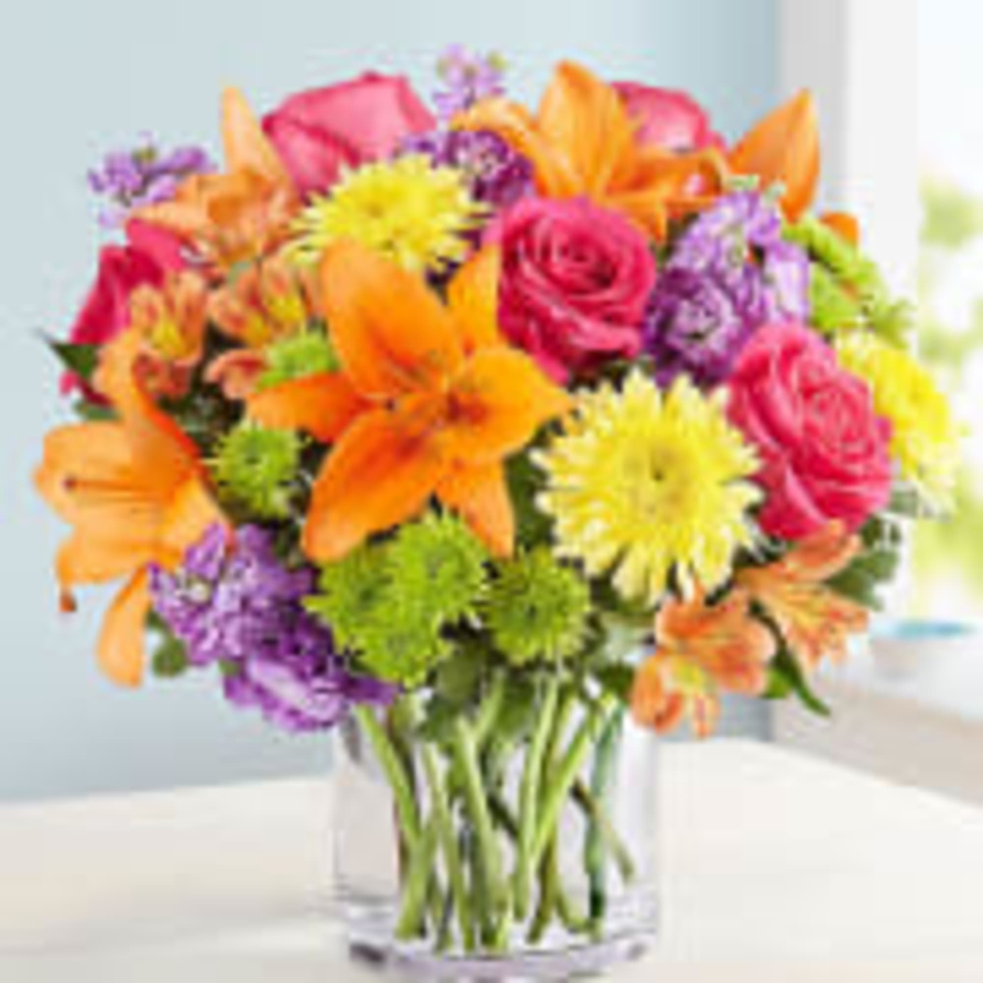 Colorful bouquet of lilies, roses, and mums in a clear glass vase