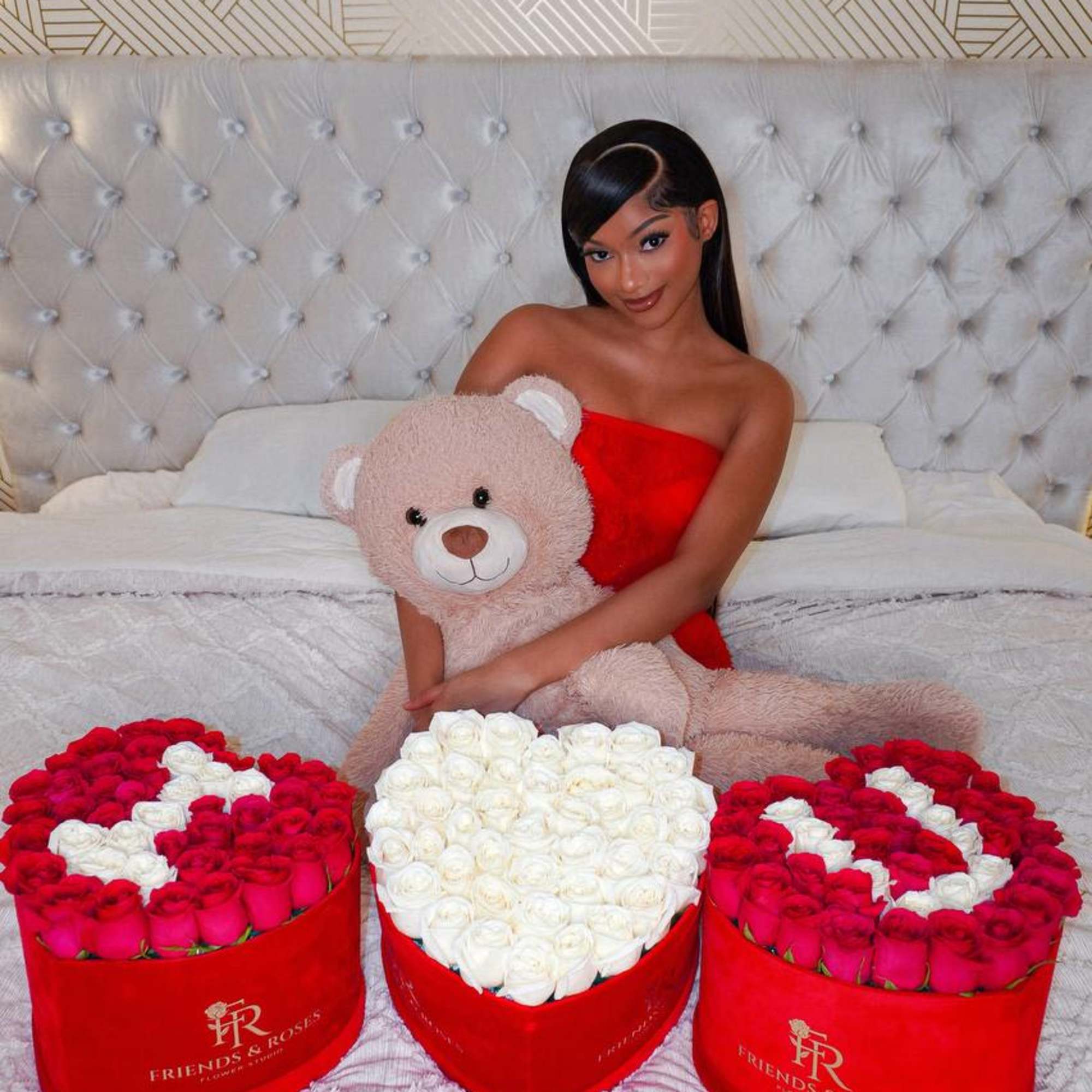 Woman holding a teddy bear with three heart-shaped rose boxes on a bed