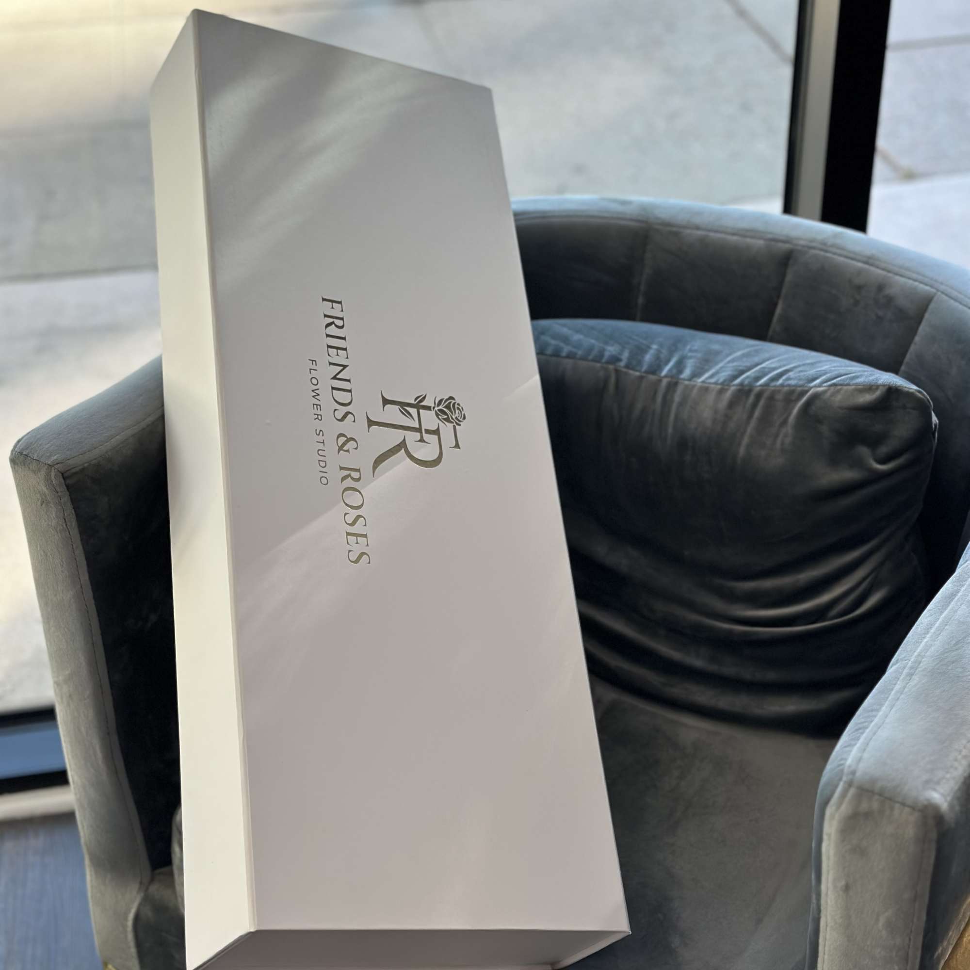 White rectangular flower box with Friends & Roses logo on a chair