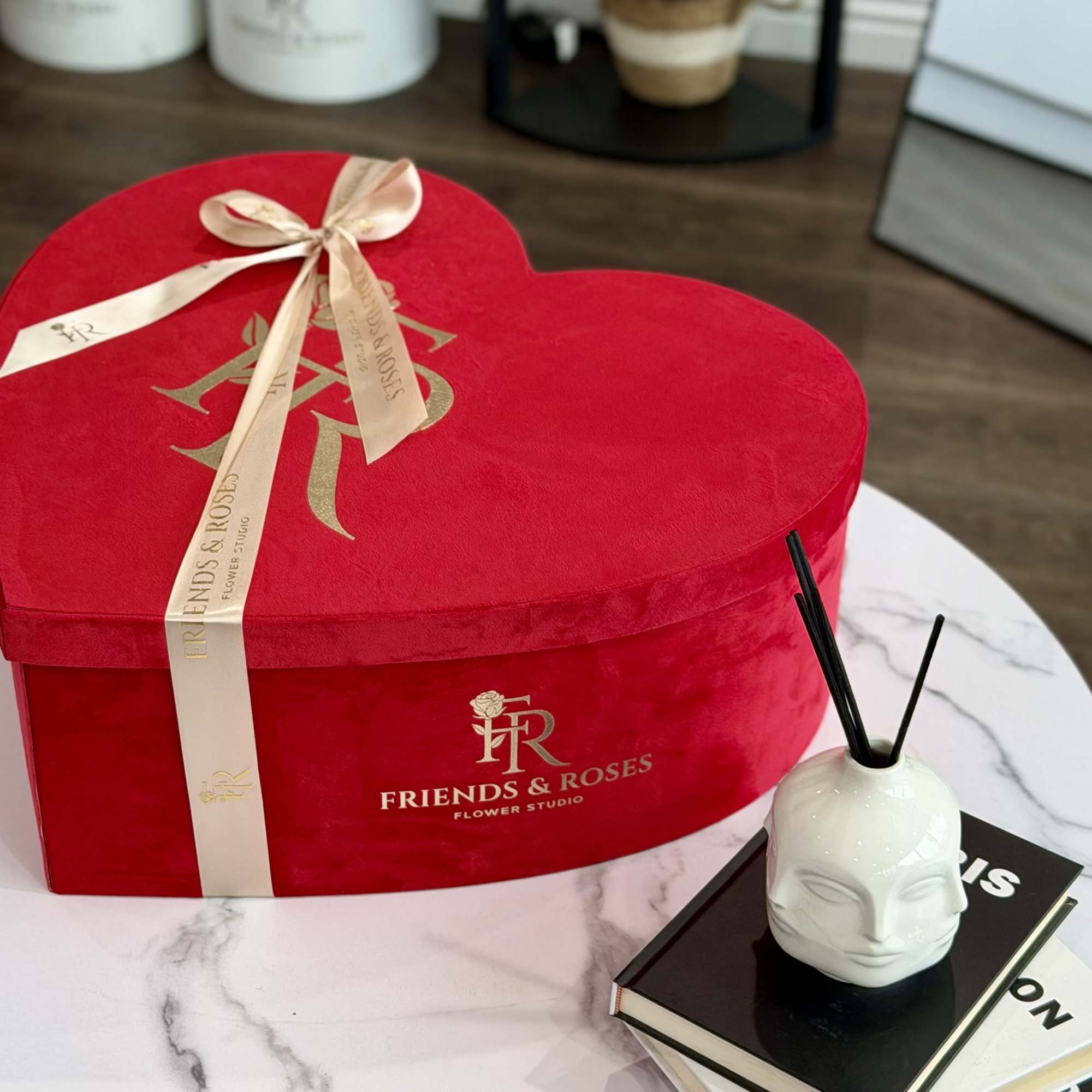 Red heart-shaped gift box with ribbon and a small ceramic diffuser on books