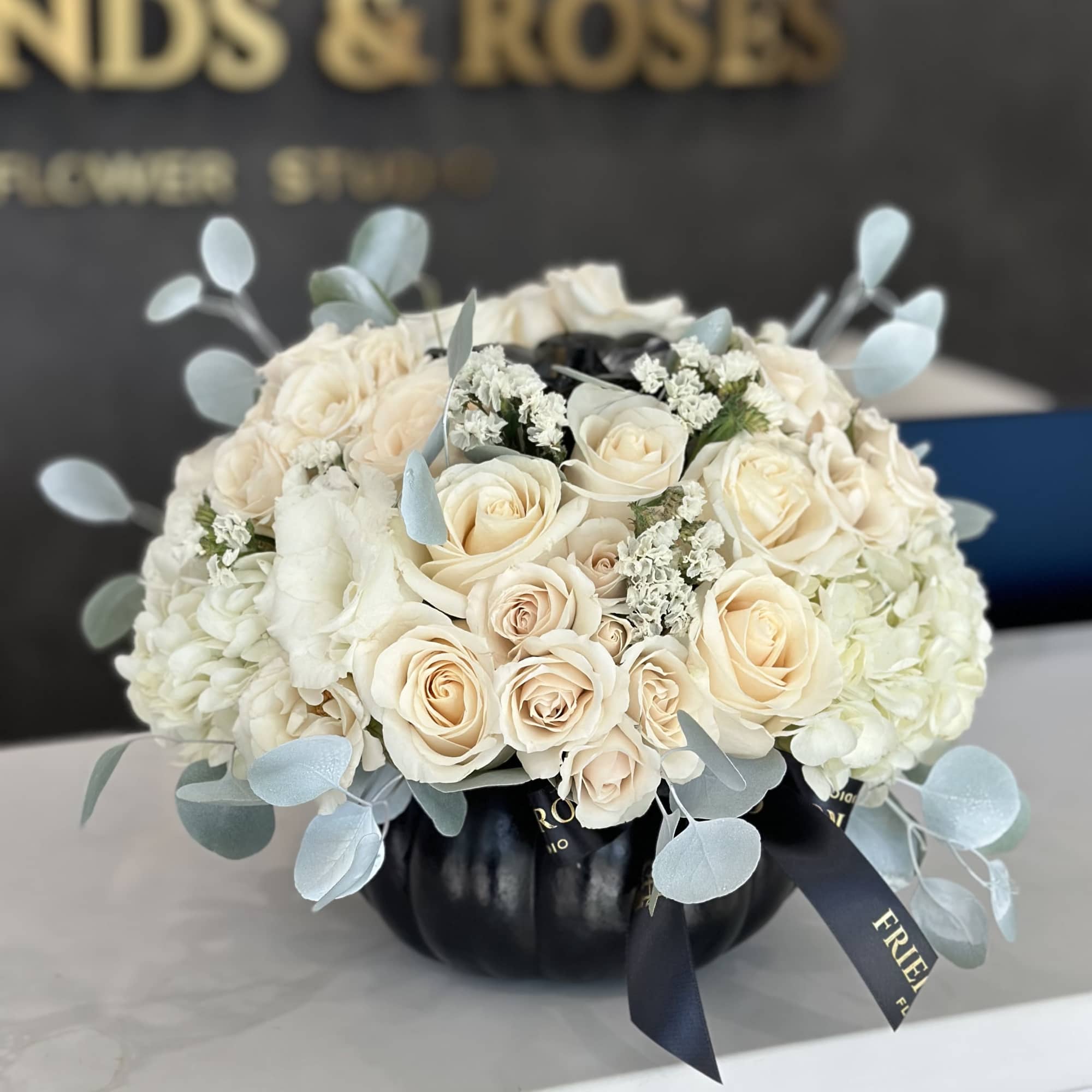 Cream roses and white hydrangeas in a black pumpkin vase with pale blue accents