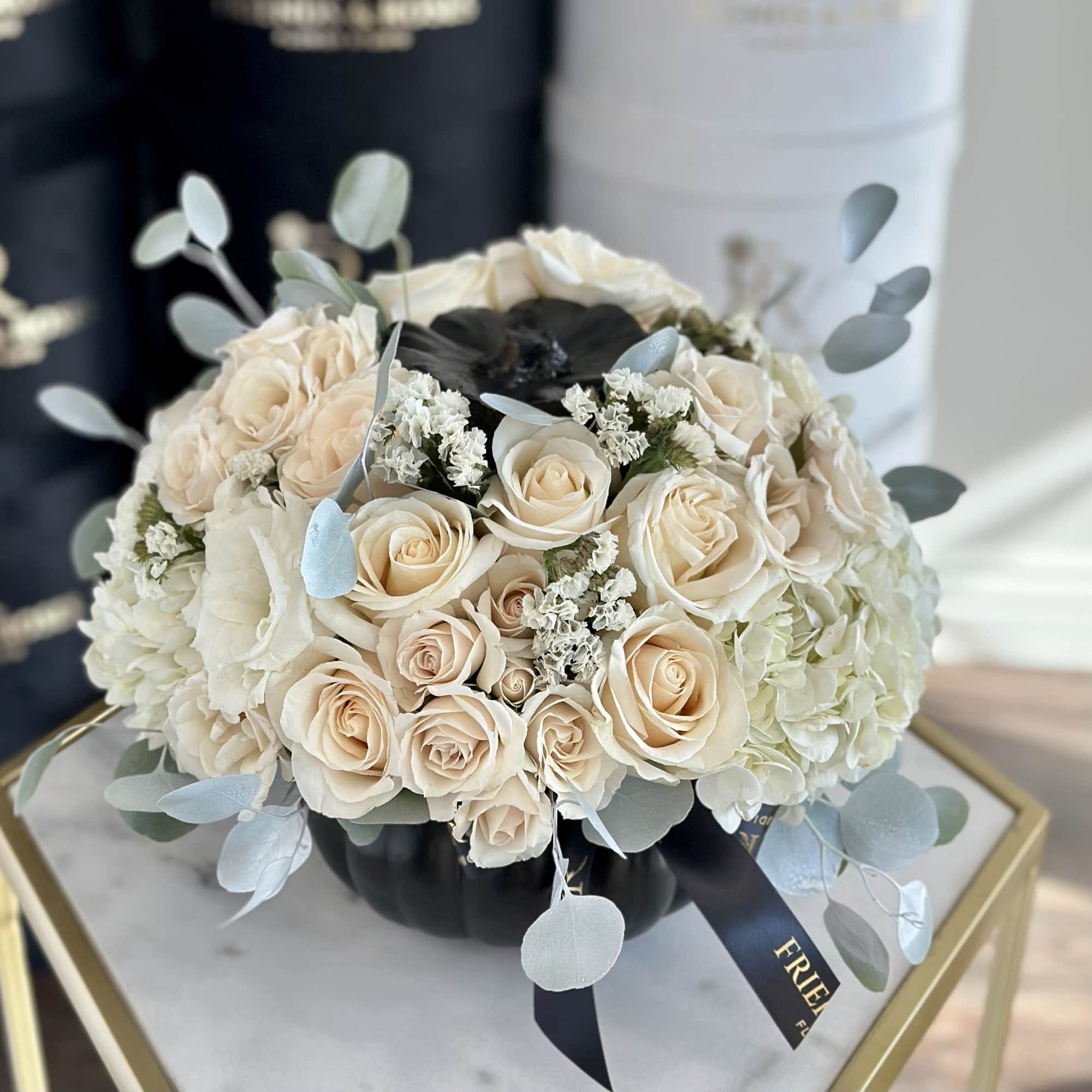 Cream rose and white hydrangea bouquet in a black box with pale blue foliage