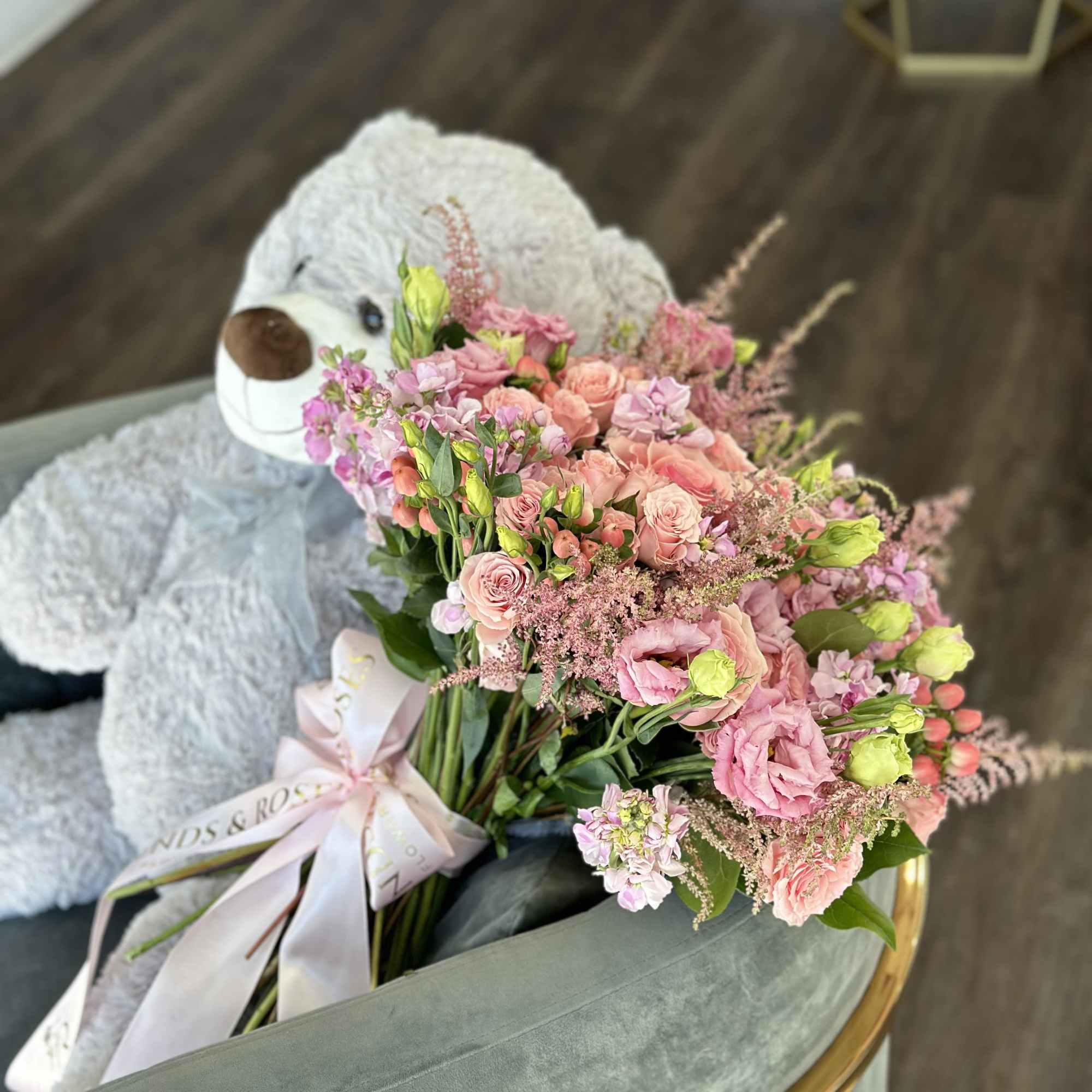 Pink bouquet with roses and lisianthus beside a large teddy bear
