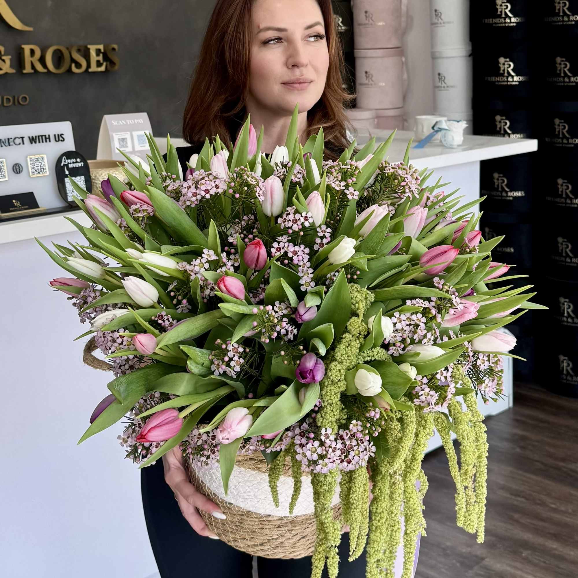 Large bouquet of pink and white tulips with small filler flowers in a woven basket