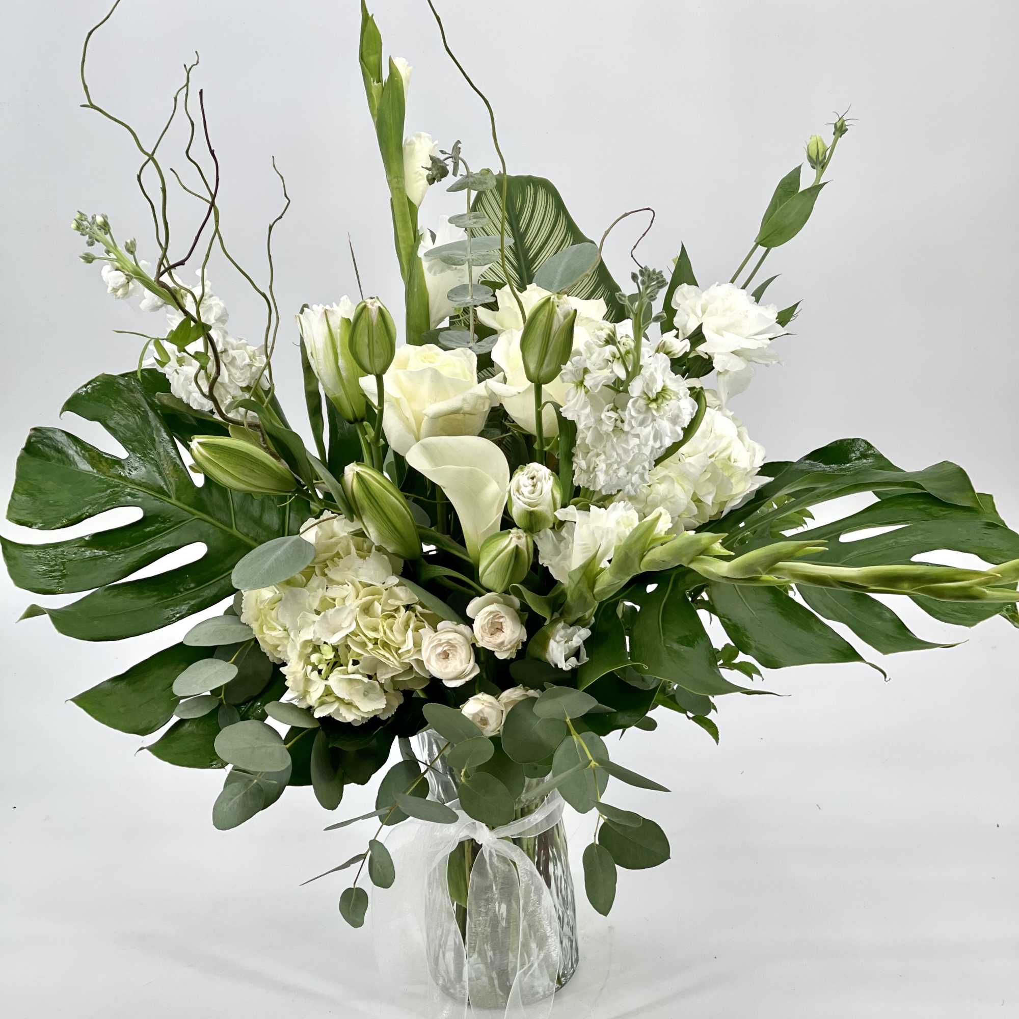 White floral arrangement in a clear glass vase with large green leaves