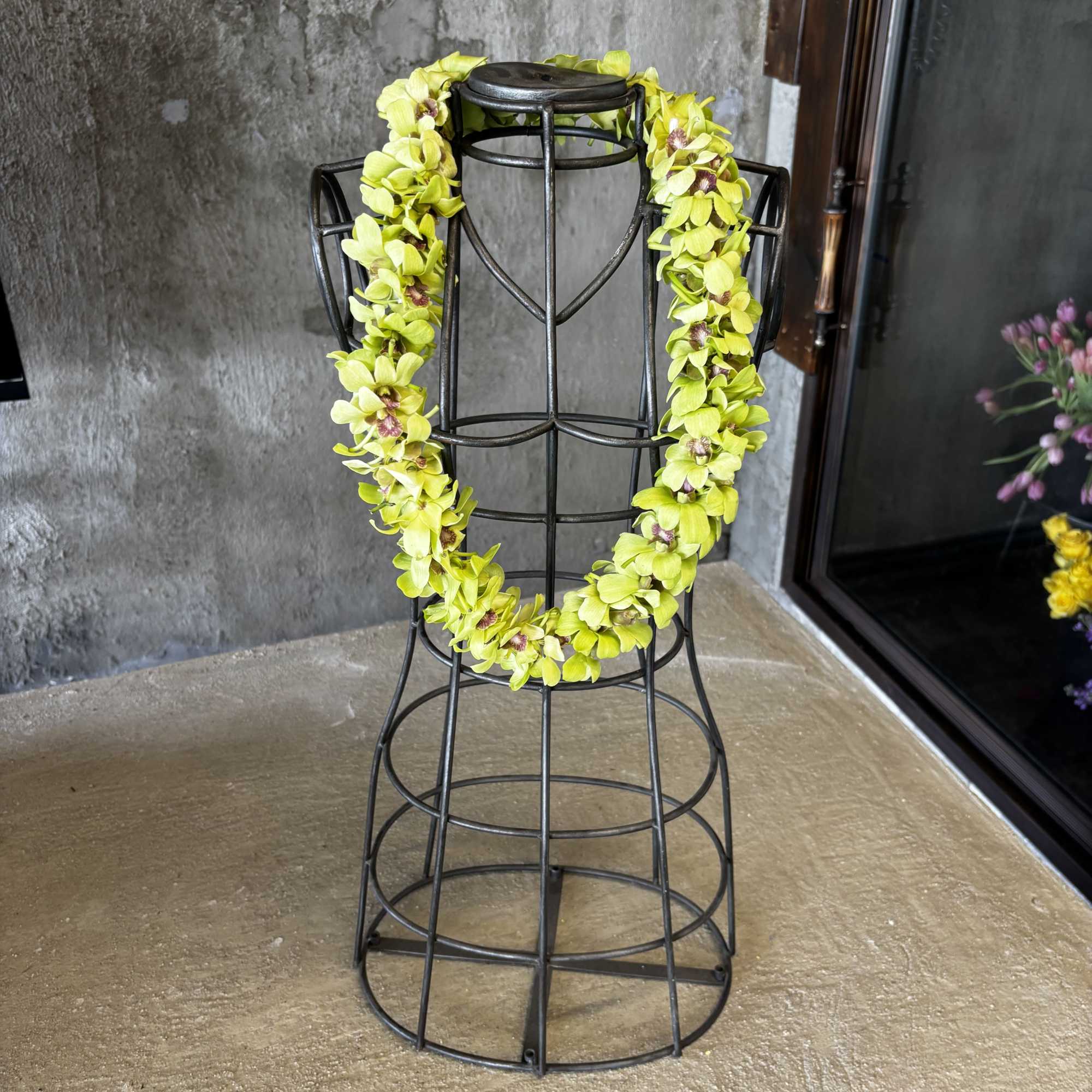 Yellow orchid lei draped over a black metal dress form