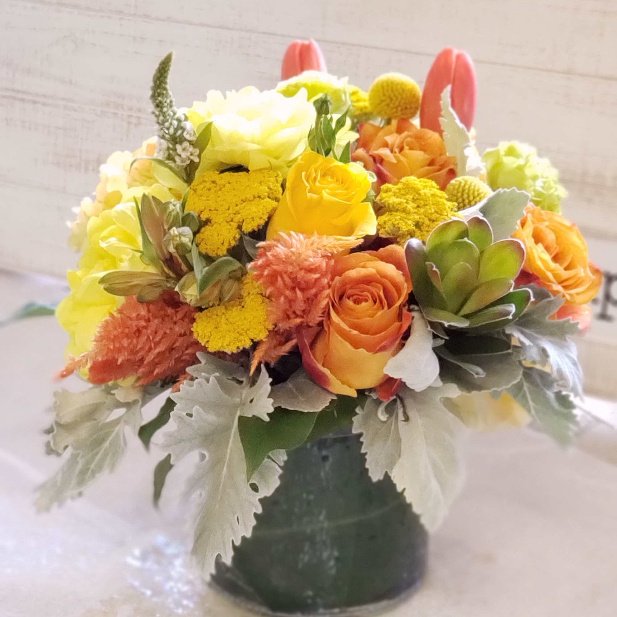 Orange and yellow flower arrangement in a dark vase with succulents