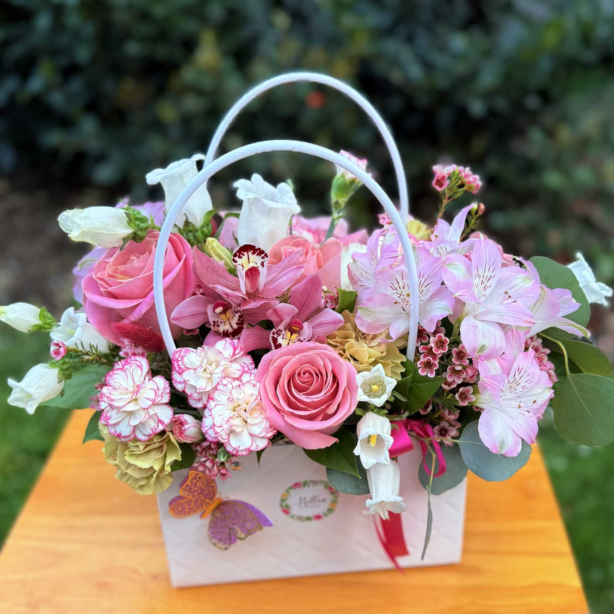 Pink and white mixed flower arrangement in a white handled gift bag