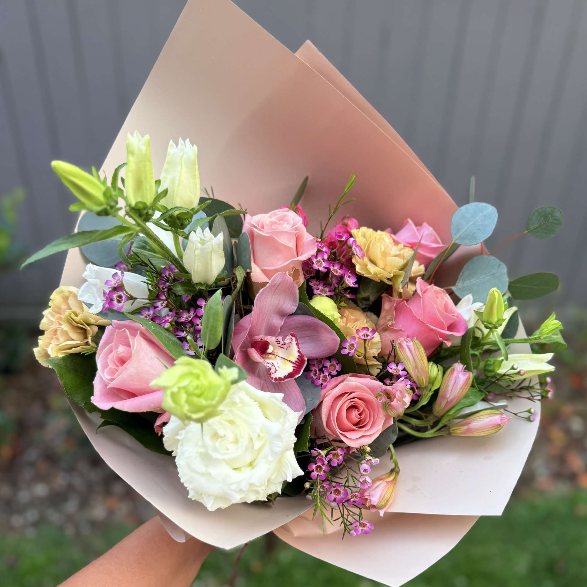 Handheld bouquet of pink and white roses with mixed blooms in blush paper