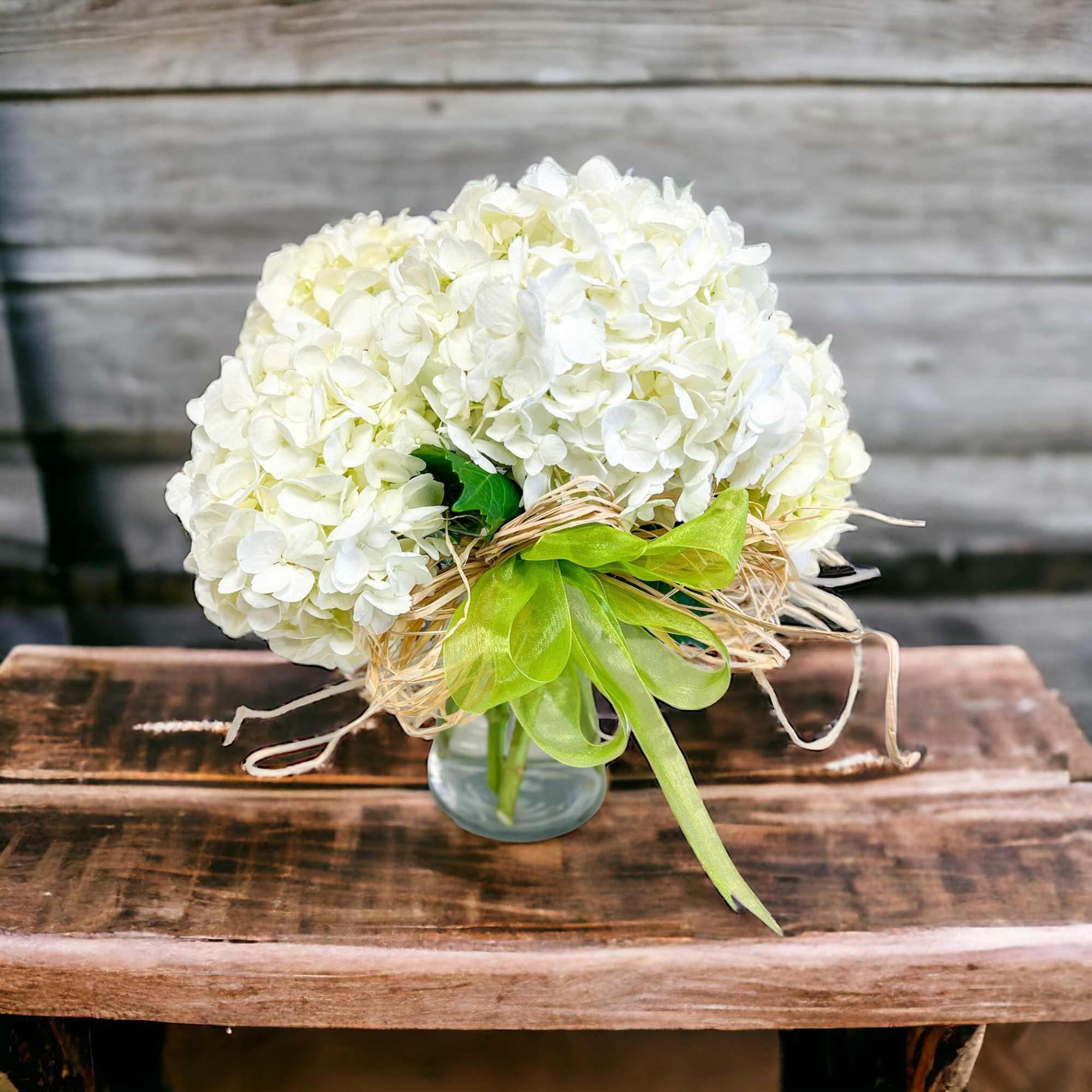 White hydrangea bouquet in a small glass vase with a green ribbon