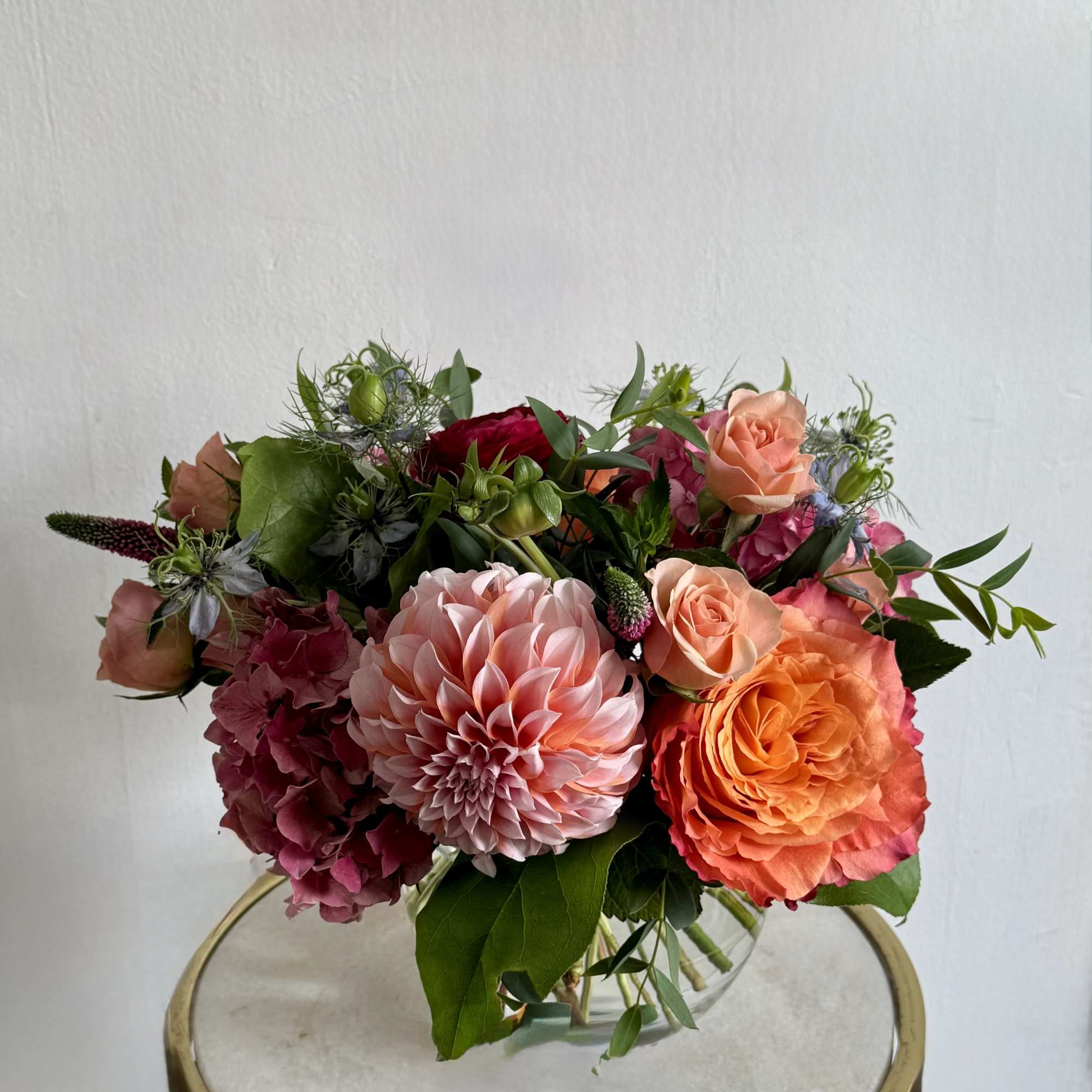 Mixed bouquet with pink dahlias, orange roses, and magenta hydrangeas in a glass vase