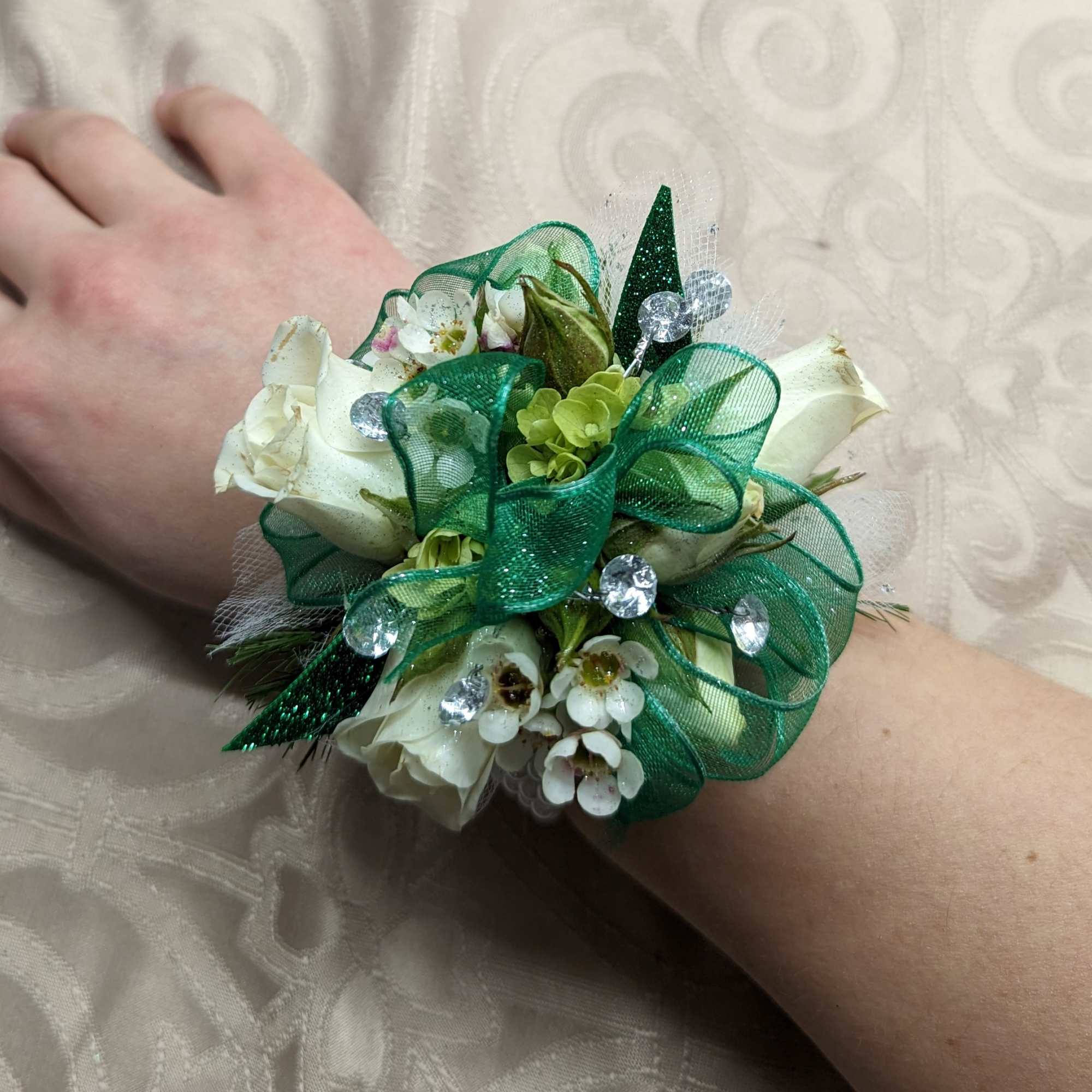 White floral wrist corsage with green ribbon and clear gems