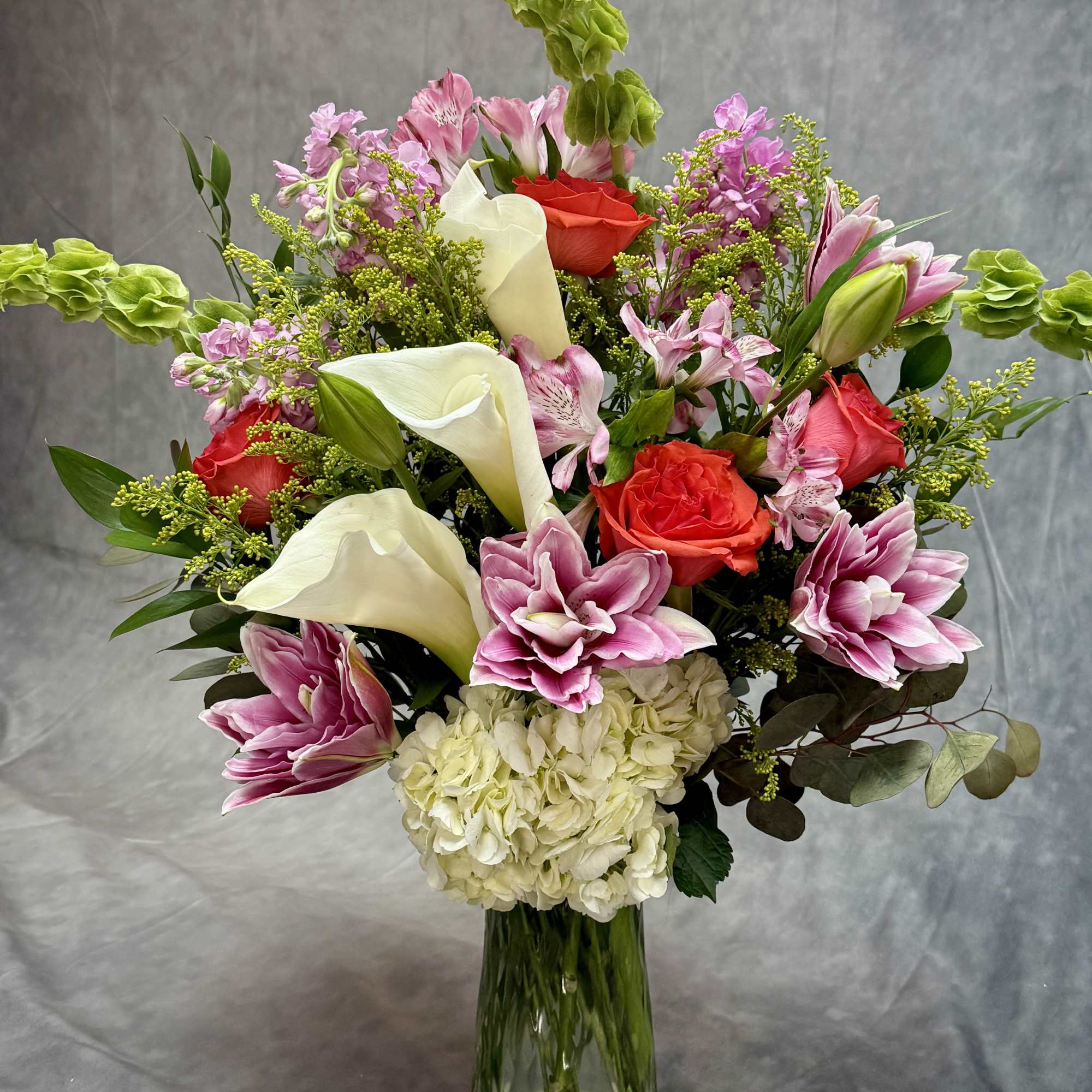 Mixed bouquet with pink lilies, red roses, white calla lilies, and hydrangea in a glass vase