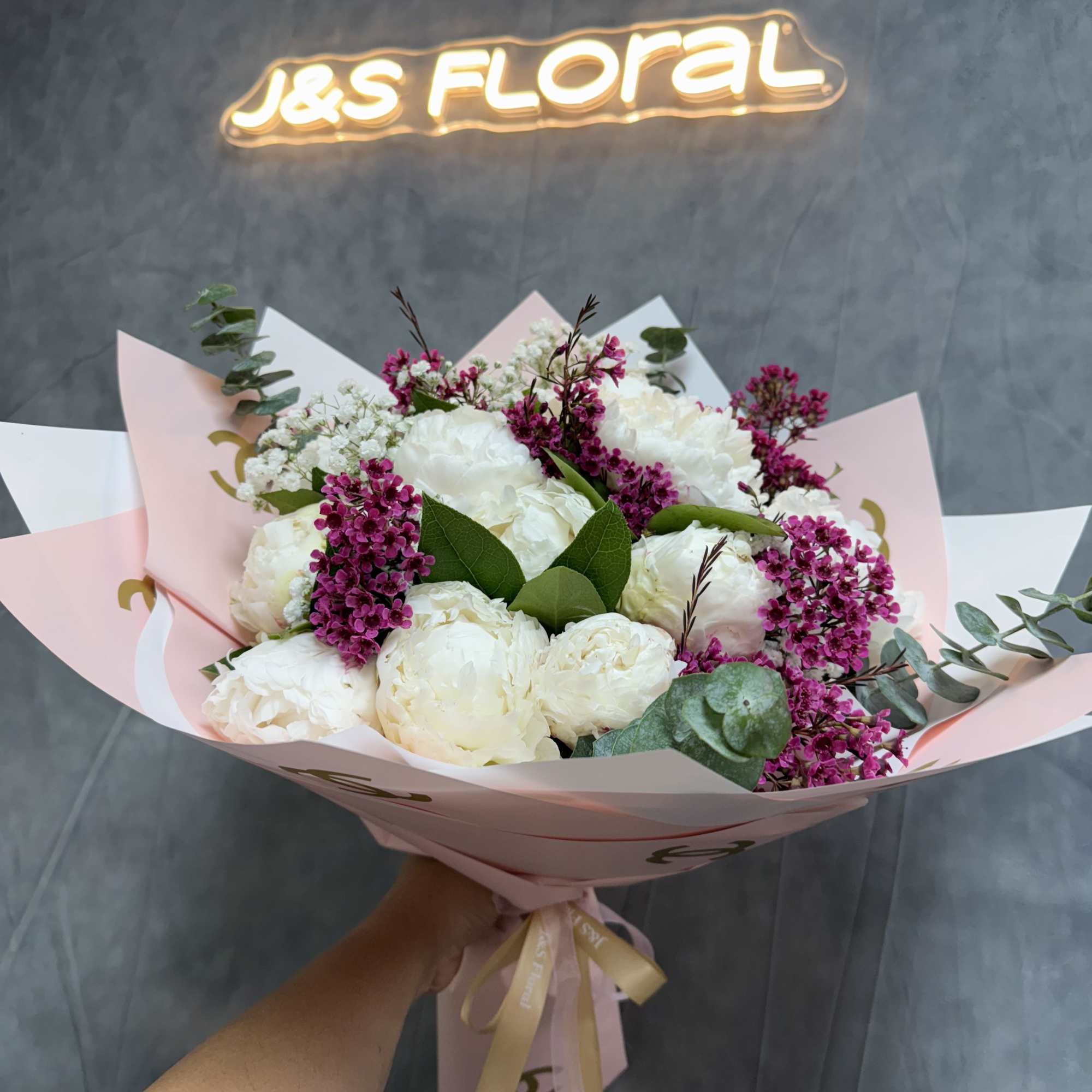 Bouquet of white peonies with magenta filler flowers in pink wrapping