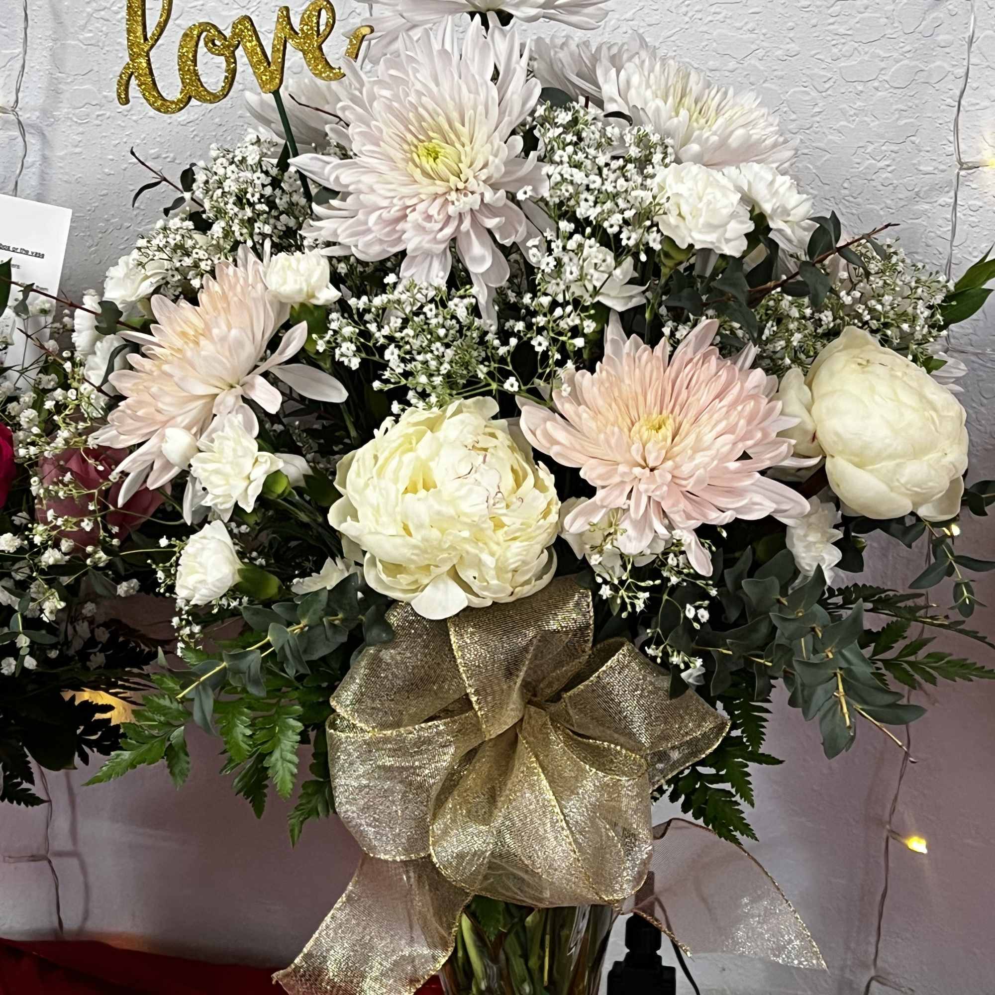 White and blush floral arrangement in a glass vase with a gold bow