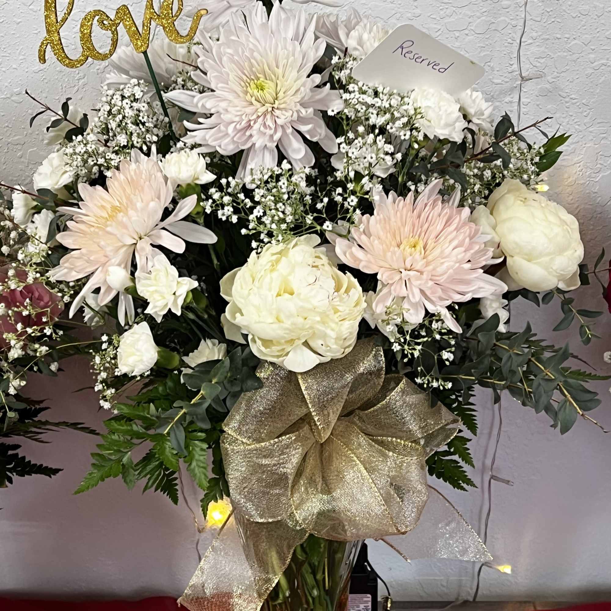 Bouquet of pale chrysanthemums and white flowers in a glass vase with a gold bow