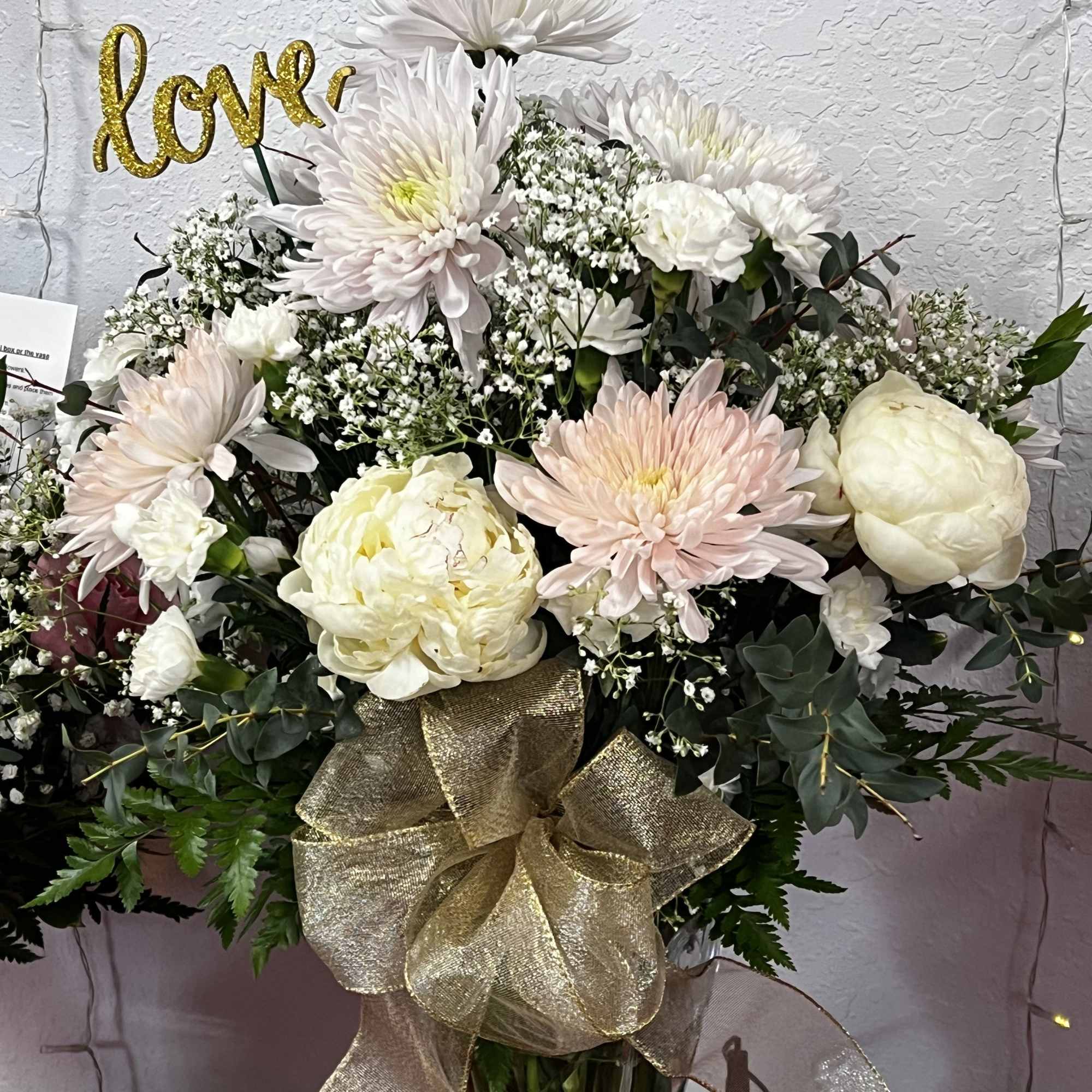 White and blush flowers in a tall glass vase with a gold ribbon