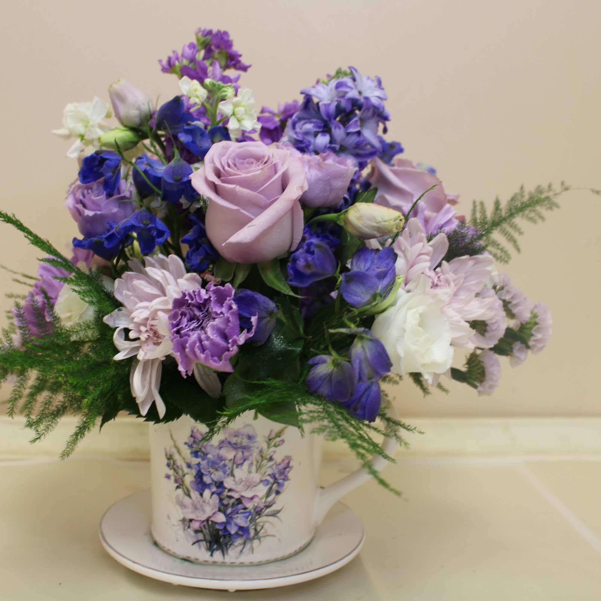 Lavender roses take center stage in this romantic teacup arrangement, a compact