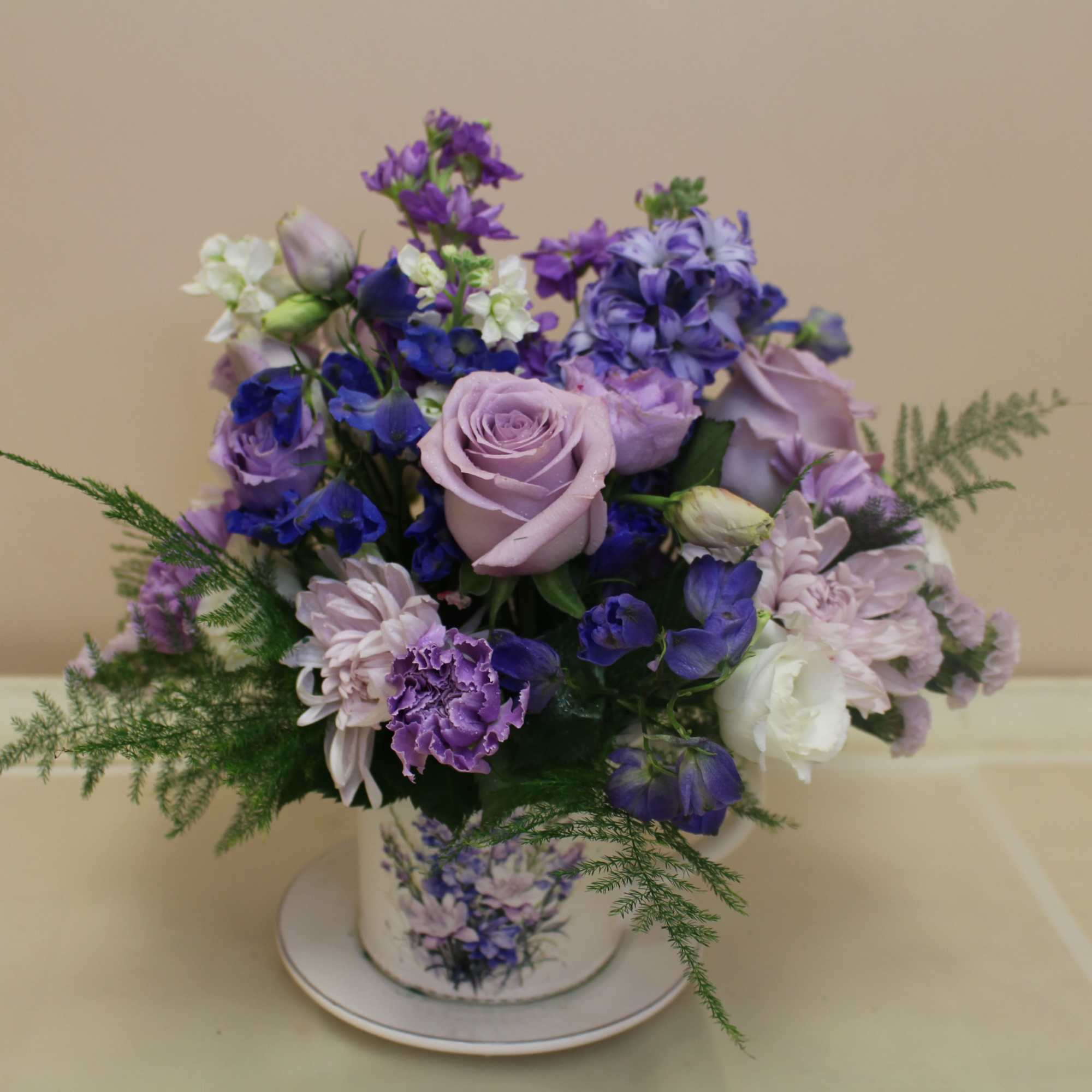 Lavender roses take center stage in this romantic teacup arrangement, a compact