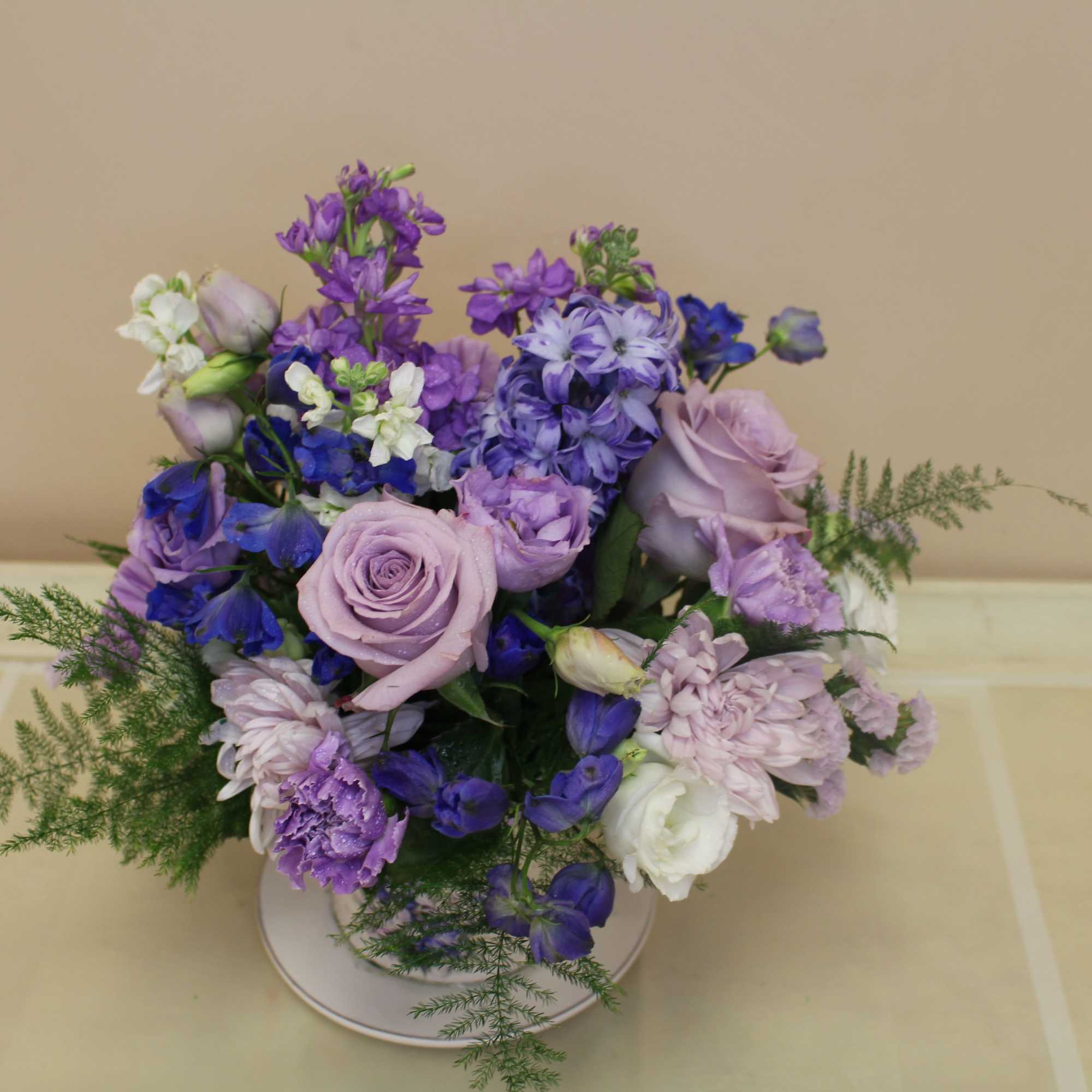 Lavender roses take center stage in this romantic teacup arrangement, a compact