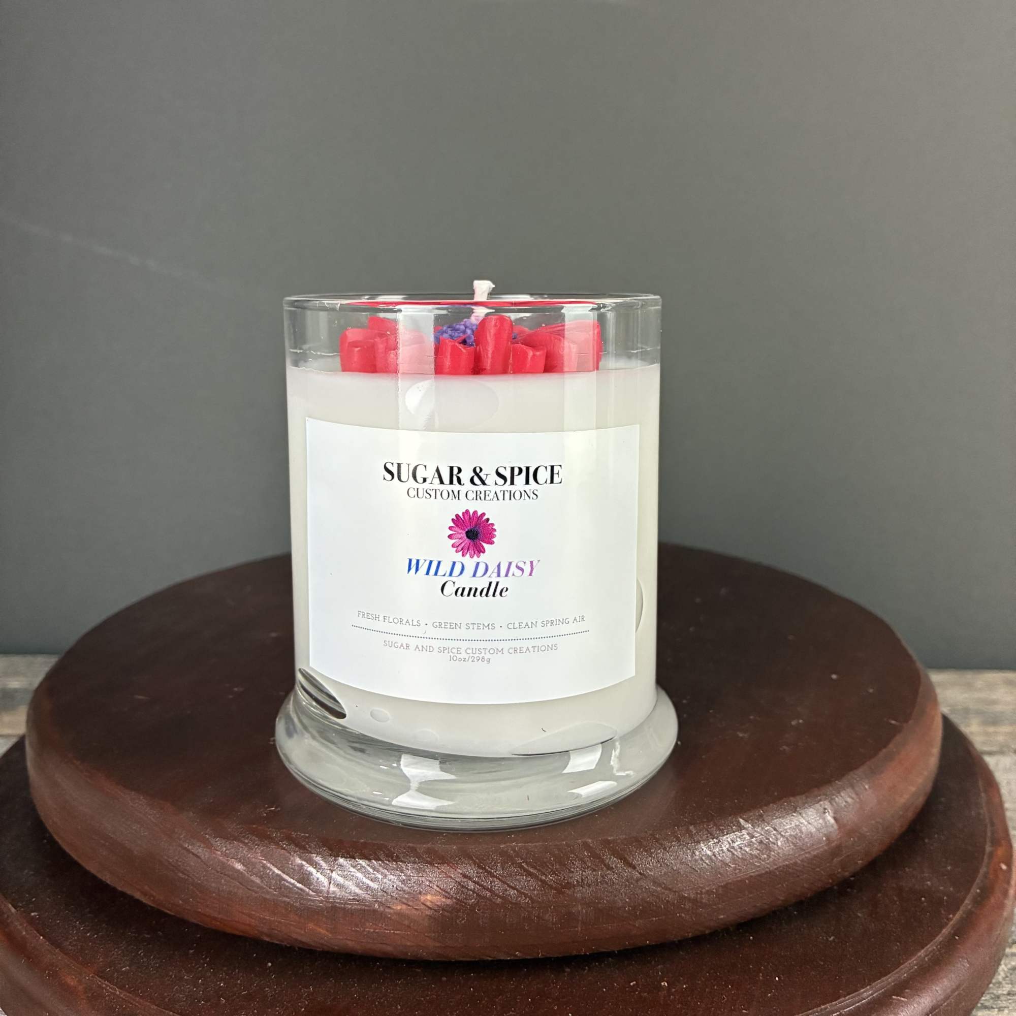 White scented candle in a clear glass jar with red wax accents on a wooden stand