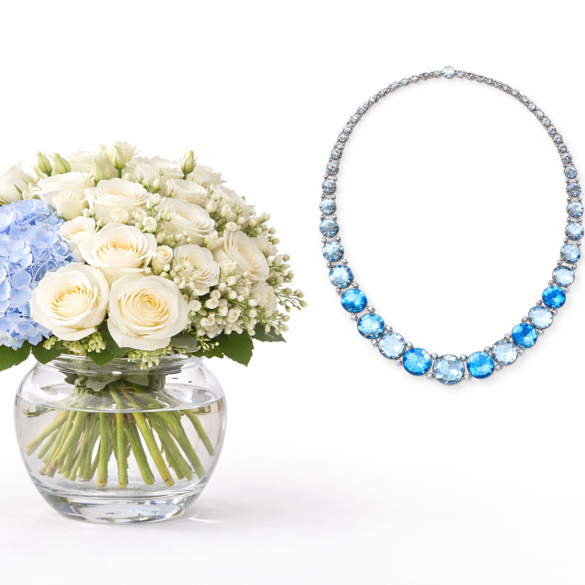 White and blue floral arrangement in a glass vase beside blue gemstone jewelry