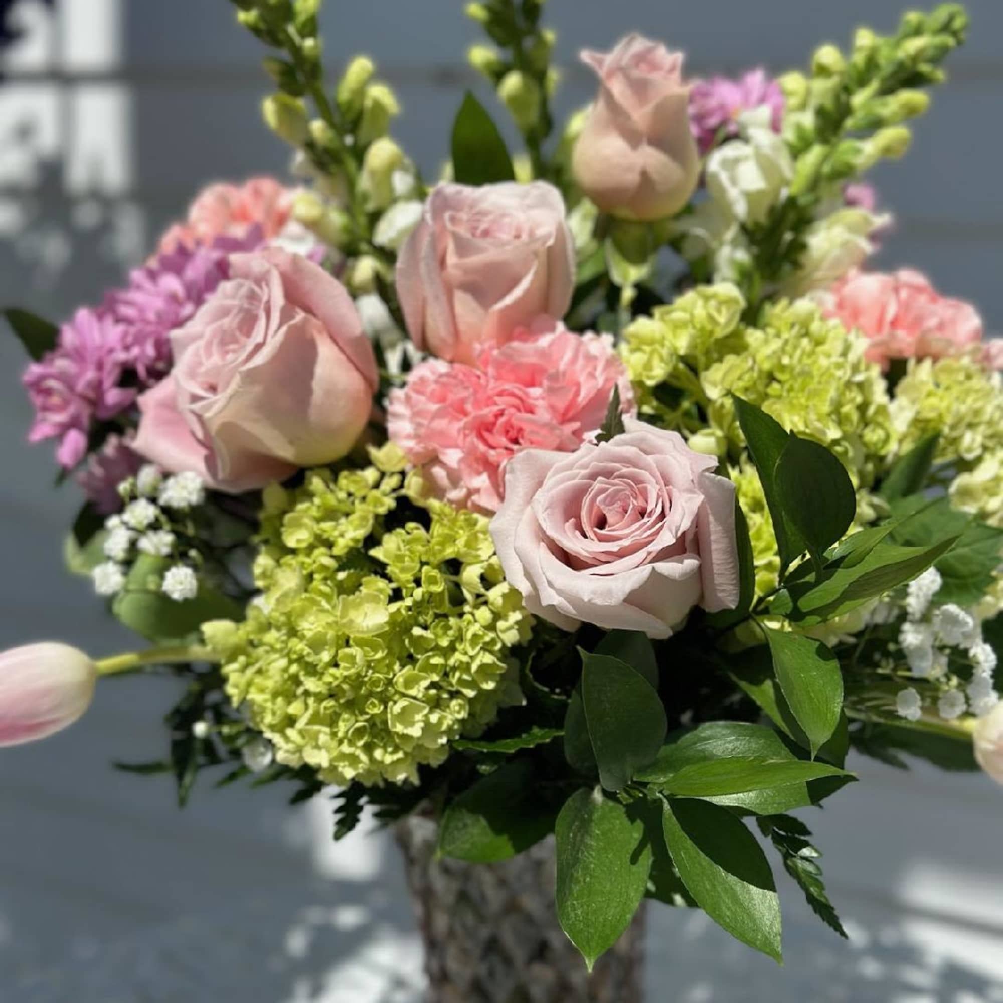 Pink roses and carnations in a glass vase with green and purple blooms