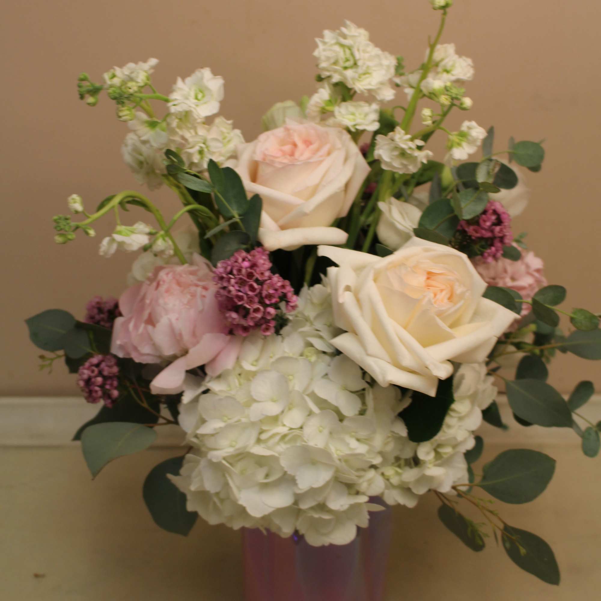 Bouquet of pale roses and white hydrangeas in a purple vase