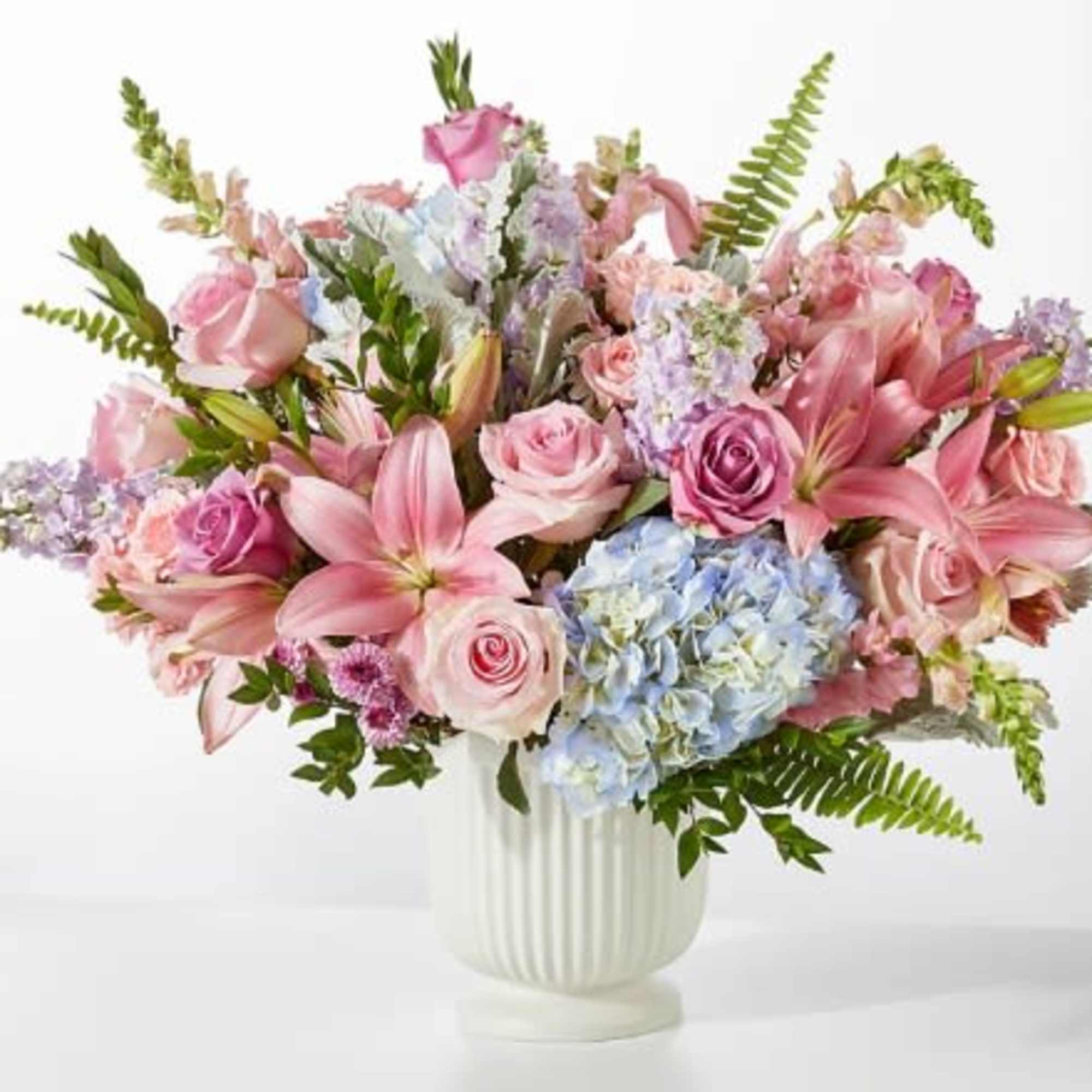 A lush, garden-style arrangement of pink lilies and roses with pale blue
