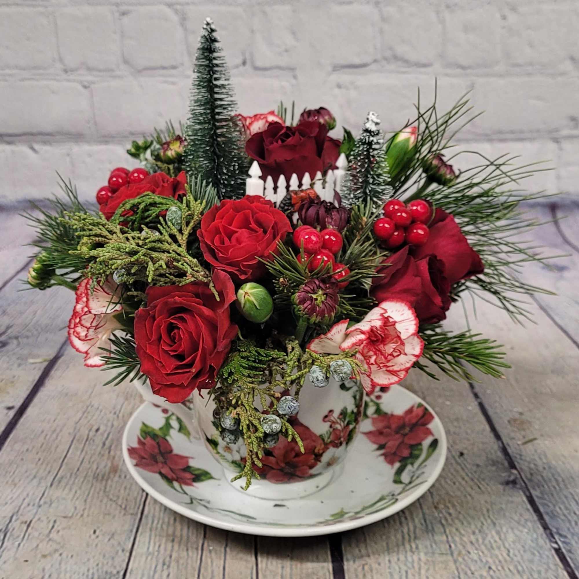Red roses and holiday greenery arranged in a teacup on a saucer