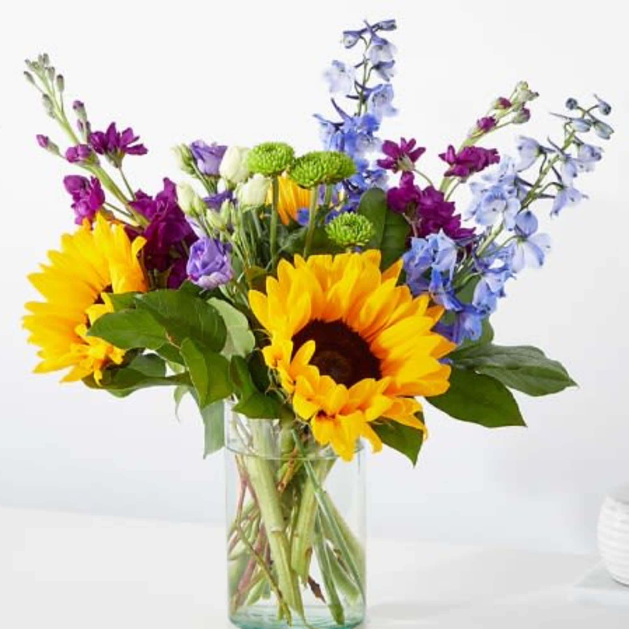 Mixed bouquet with sunflowers, purple and blue flowers in a clear glass vase